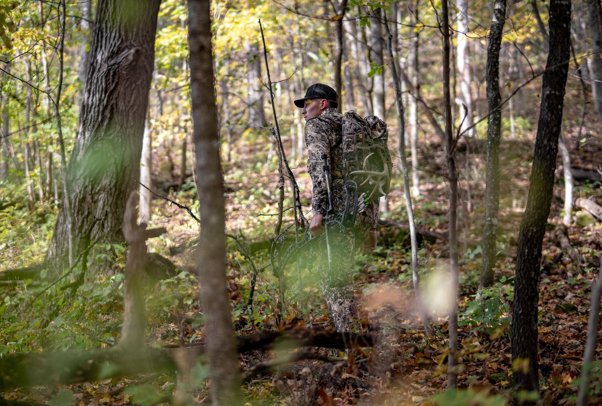 A hunter in the woods with a gear pack and bow.