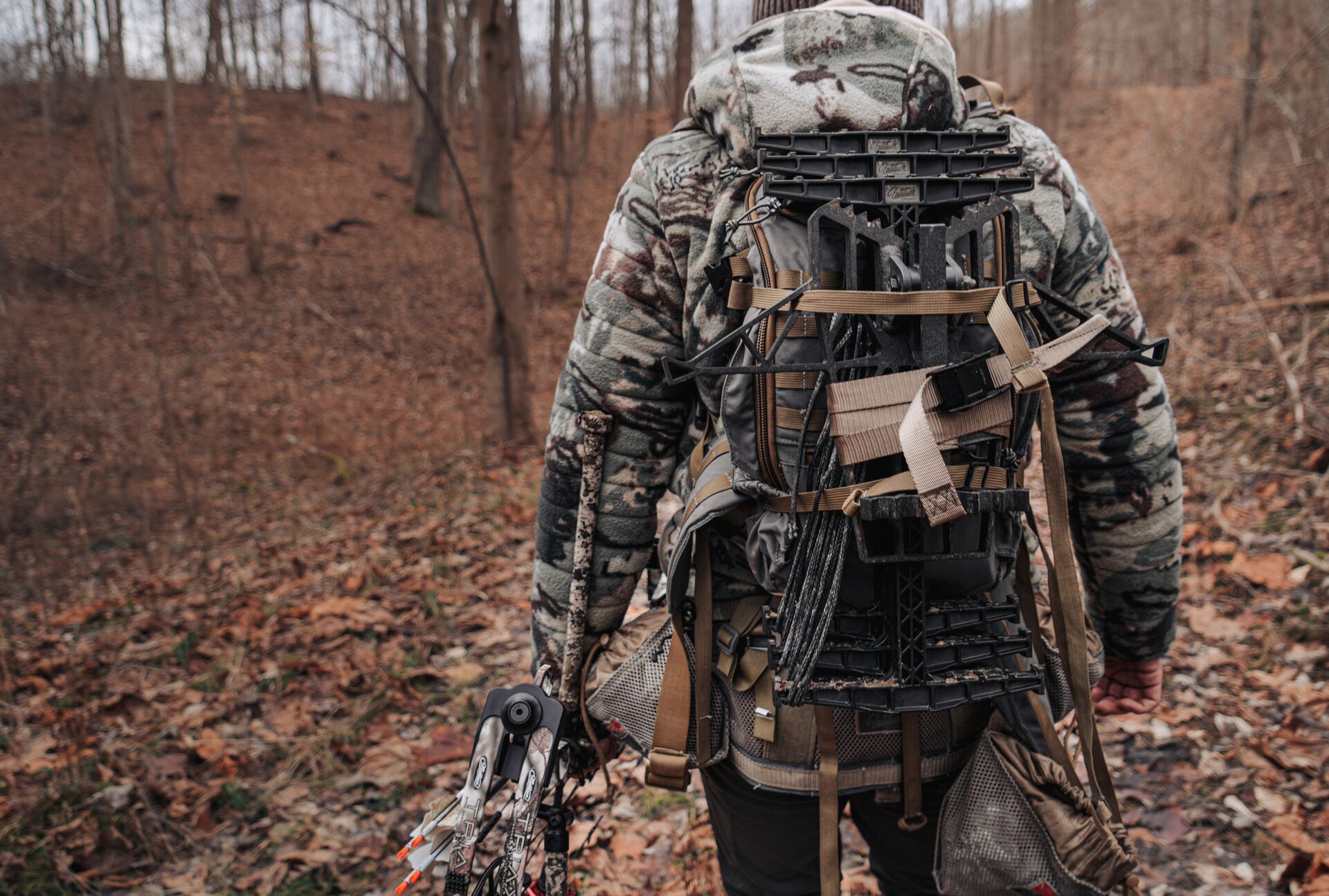 A hunter in camo carrying a bow through the woods, Tennessee hunting concept.