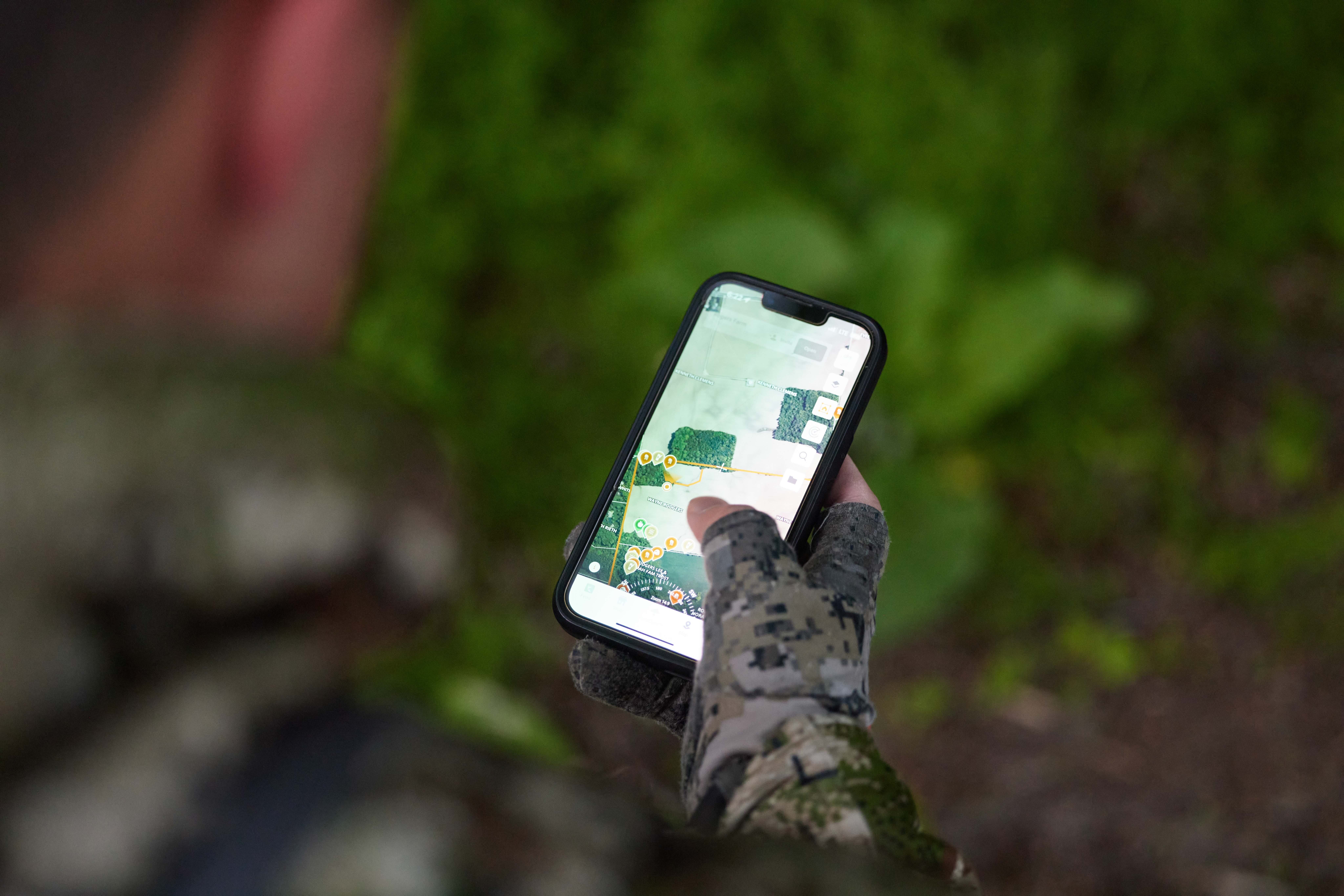 Close-up of a hand holding a phone showing the HuntWise app on screen, understanding and mapping deer sounds concept.