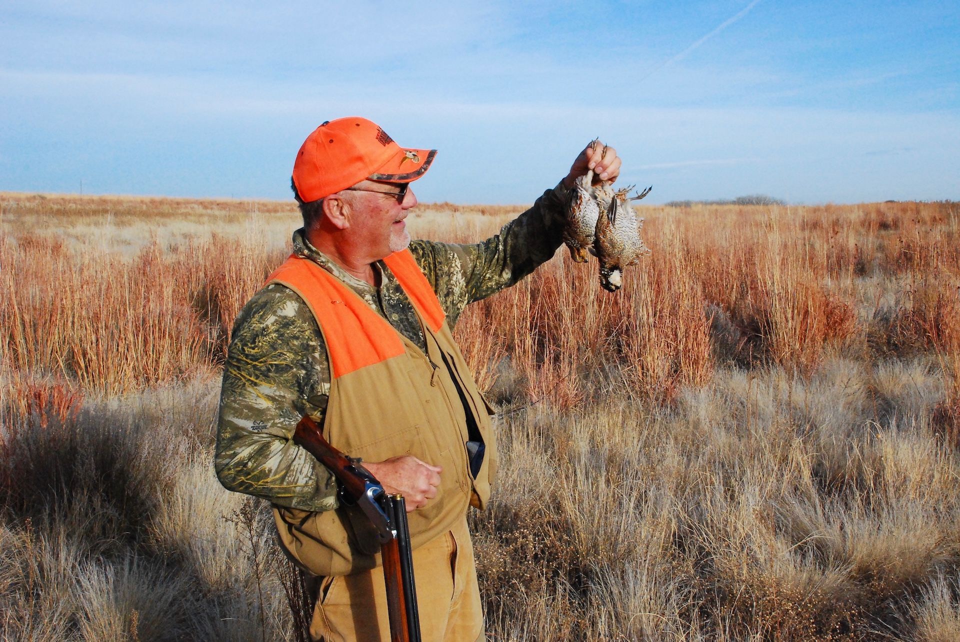 Hunter holds up two quail after hunt, calling quail concept.