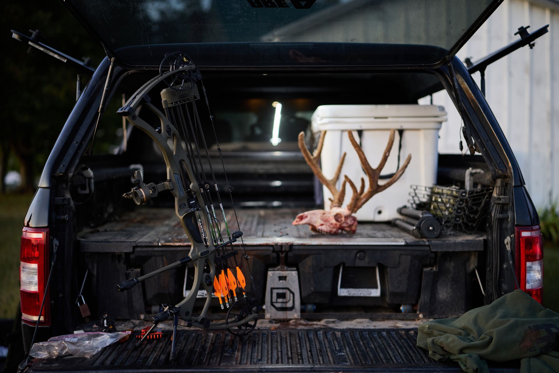 Bow leans against SUV tailgate with deer skull nearby, archery equipment care concept.
