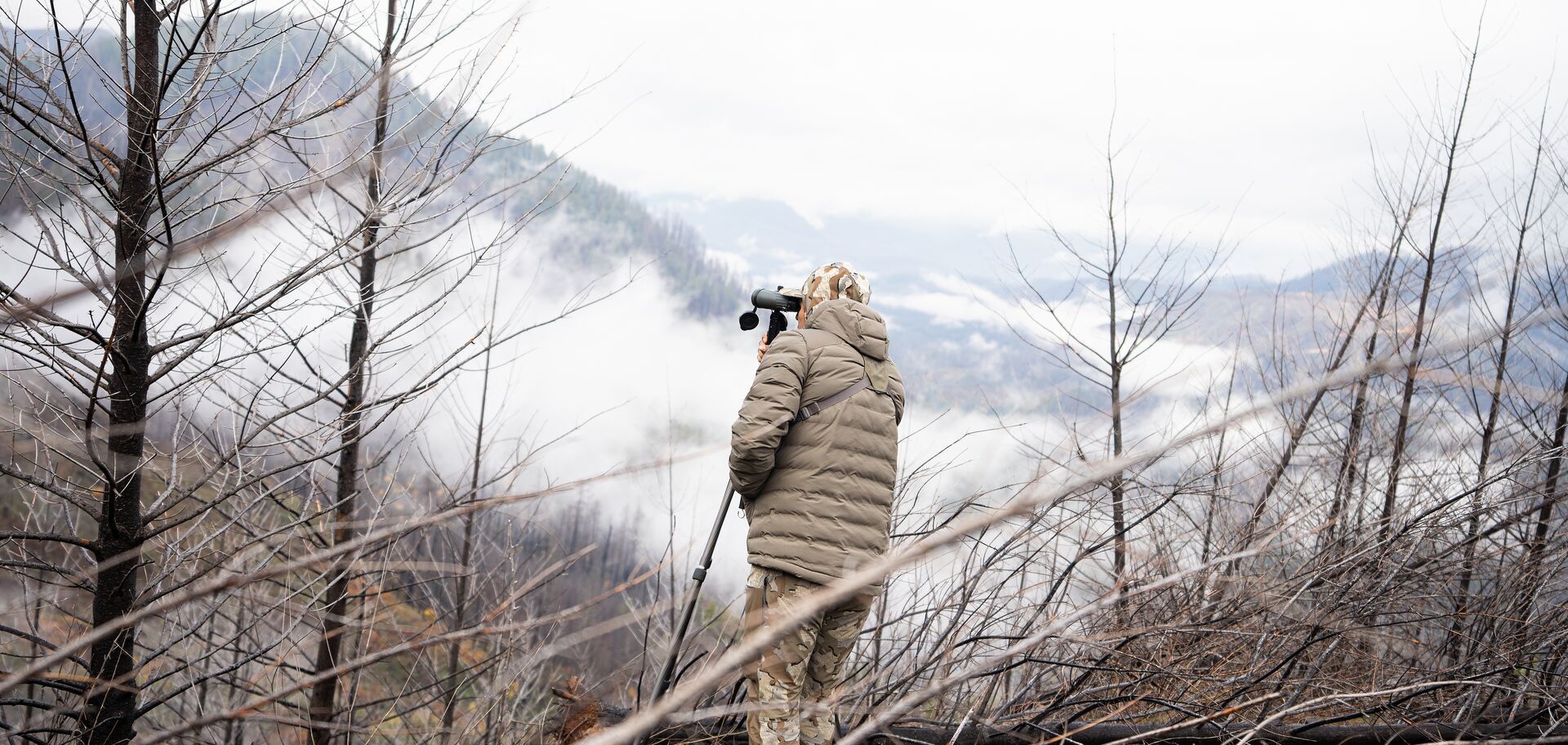 Hunter using spotting scope on mountain, big game hunts concept.