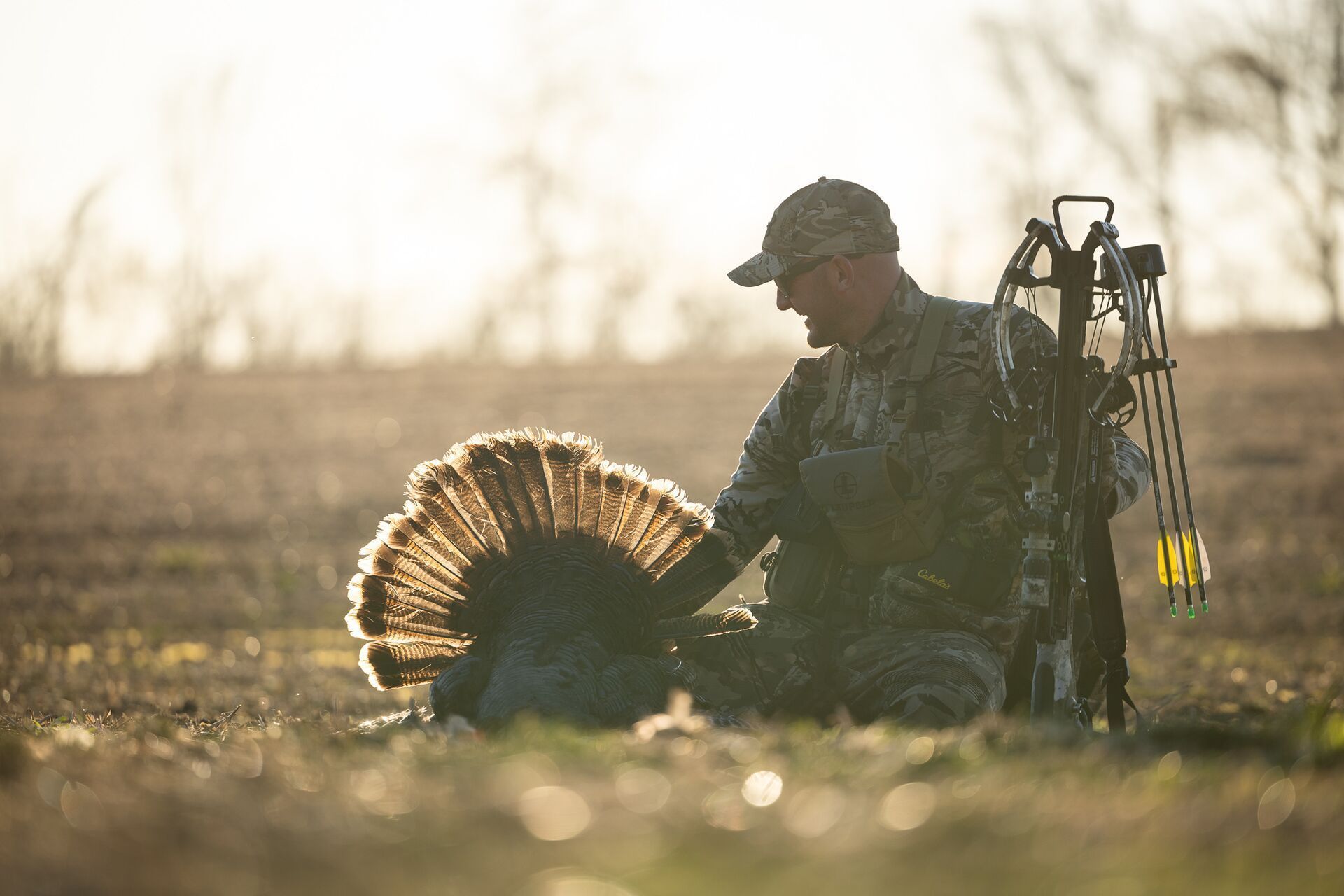 Hunter with a bow next to turkey on ground after hunt, Wisconsin turkey hunting season concept.