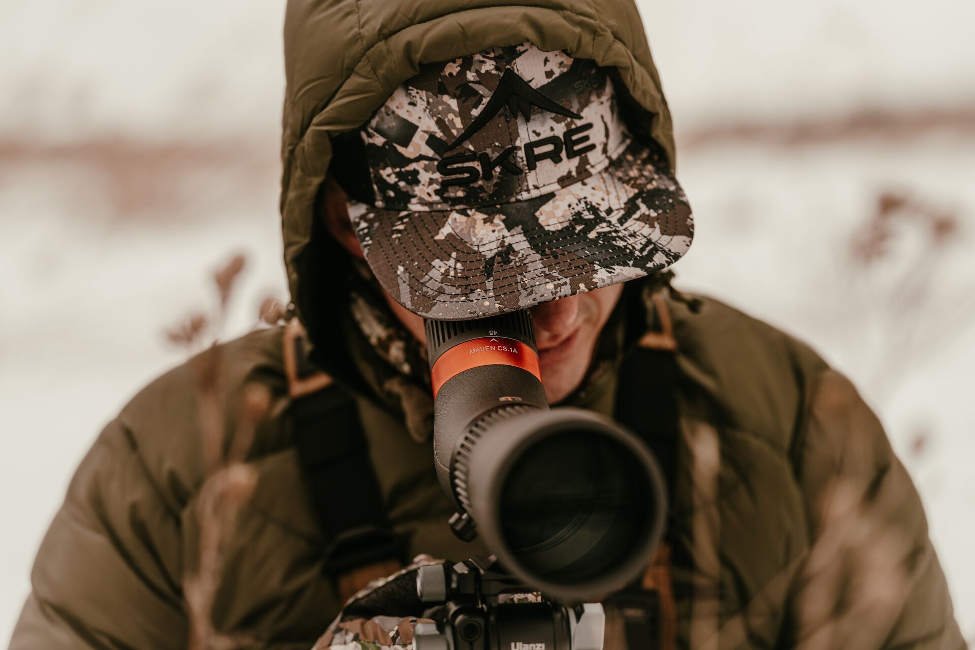 A hunter in a coat uses a scope for glassing, Montana hunting seasons concept.