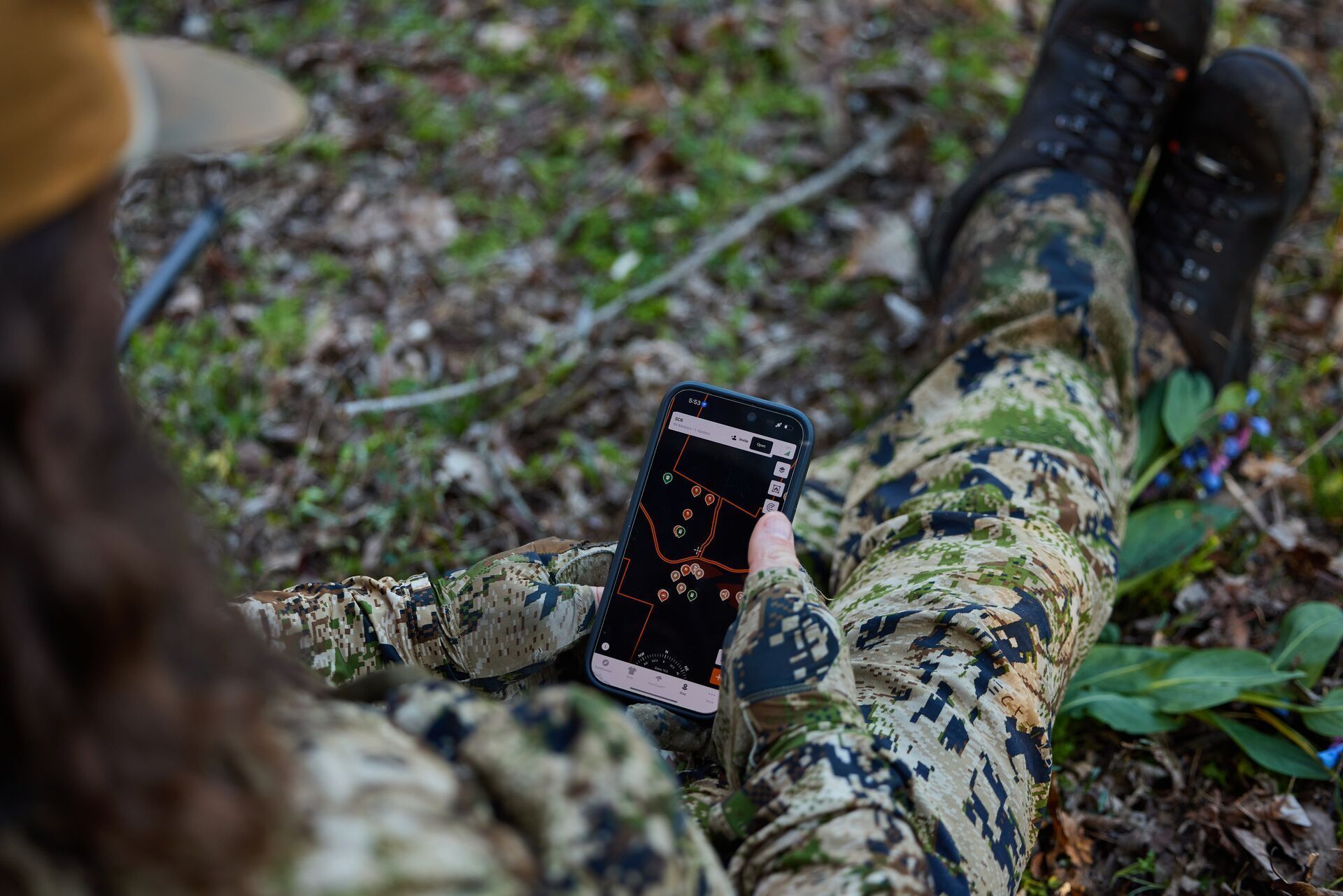 A hunter sits in the field looking at a phone using the HuntWise hunting app.