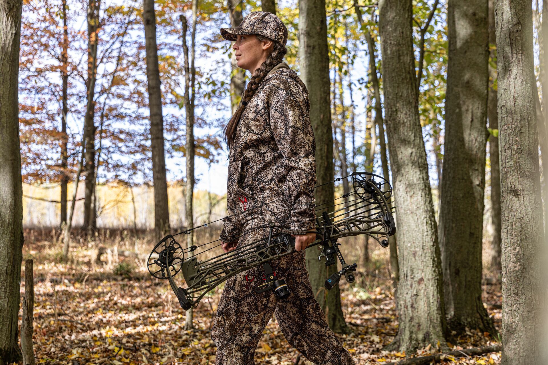 A female hunter carries a bow and arrows in the woods.