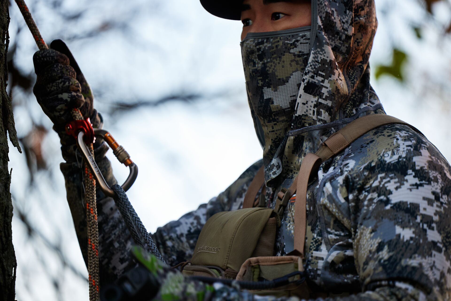 A hunter in cold weather gear in a tree saddle.