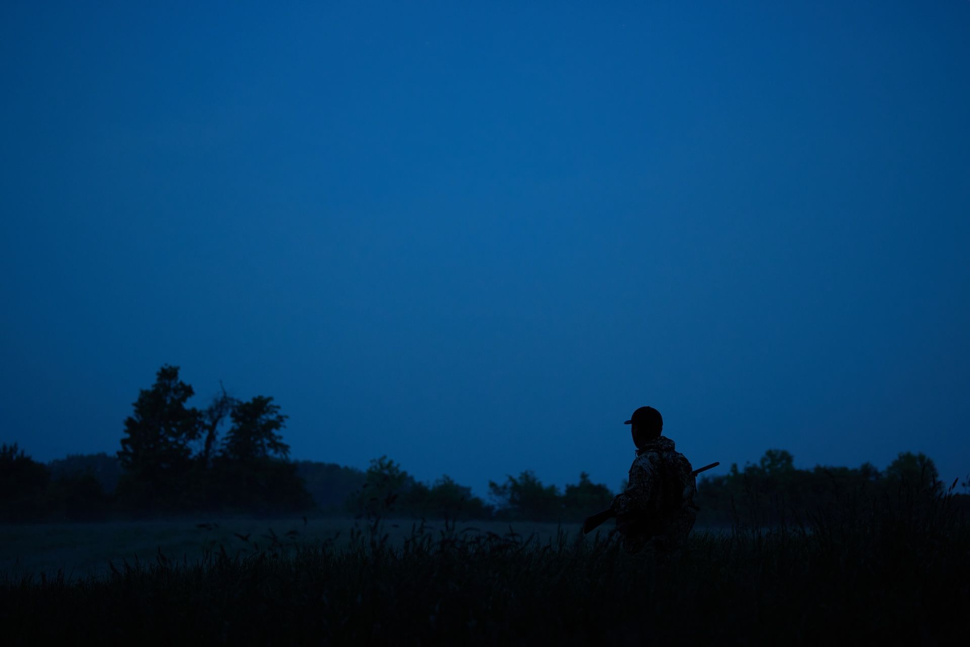 A hunter with a rifle in a field for night hunting.