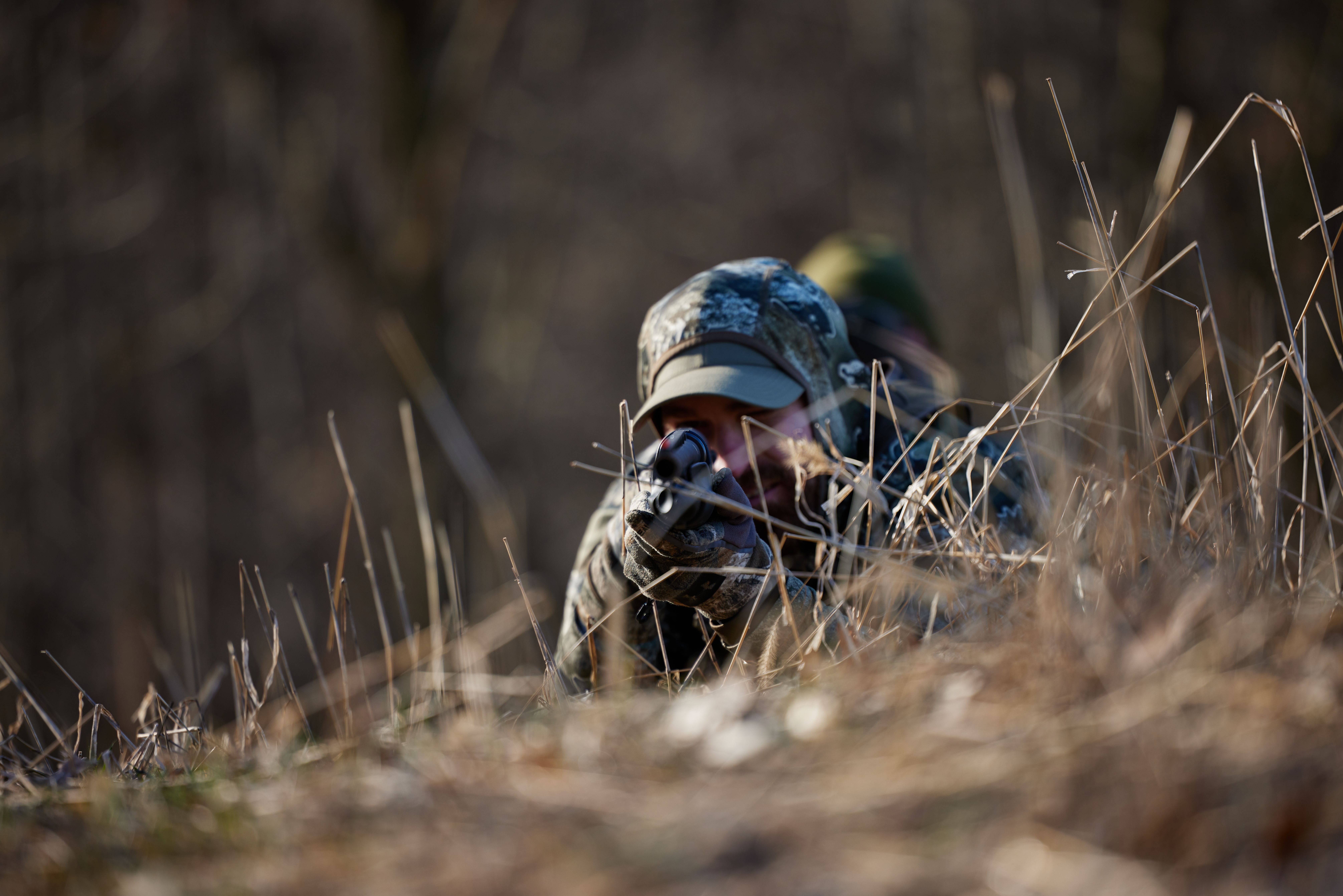 A hunter lays on the ground aiming a firearm, rifle v shotgun concept.