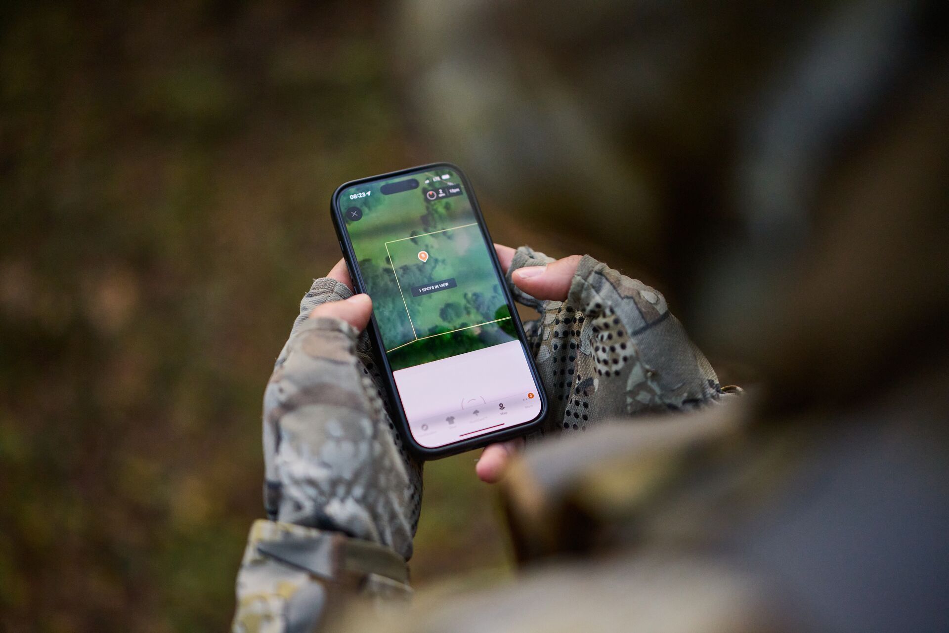 Close-up hunter holds phone showing HuntWise terrain layer.