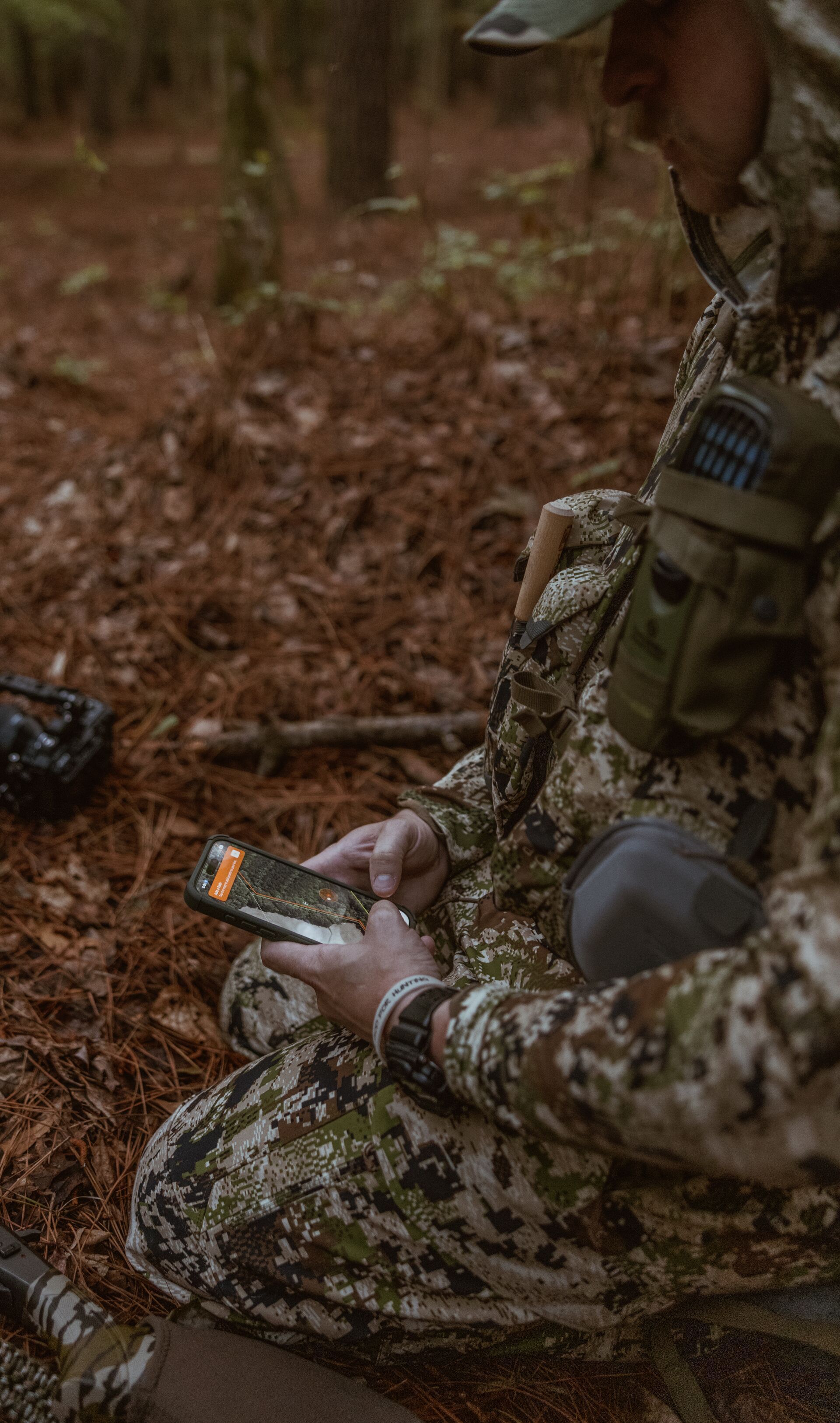 Hunter kneeling in the woods using HuntWise on a phone.