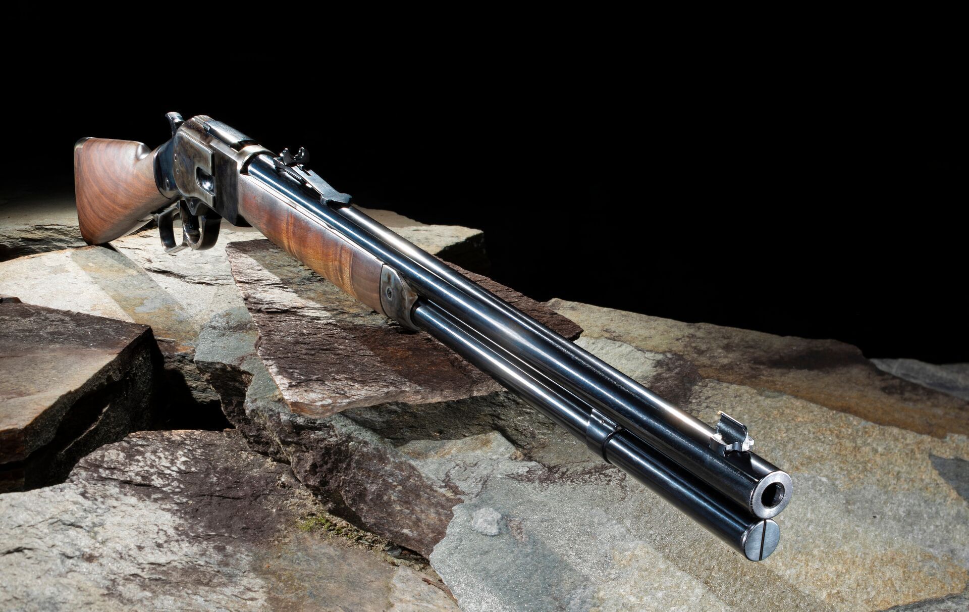 A lever action rifle sits on stone in front of a black background.