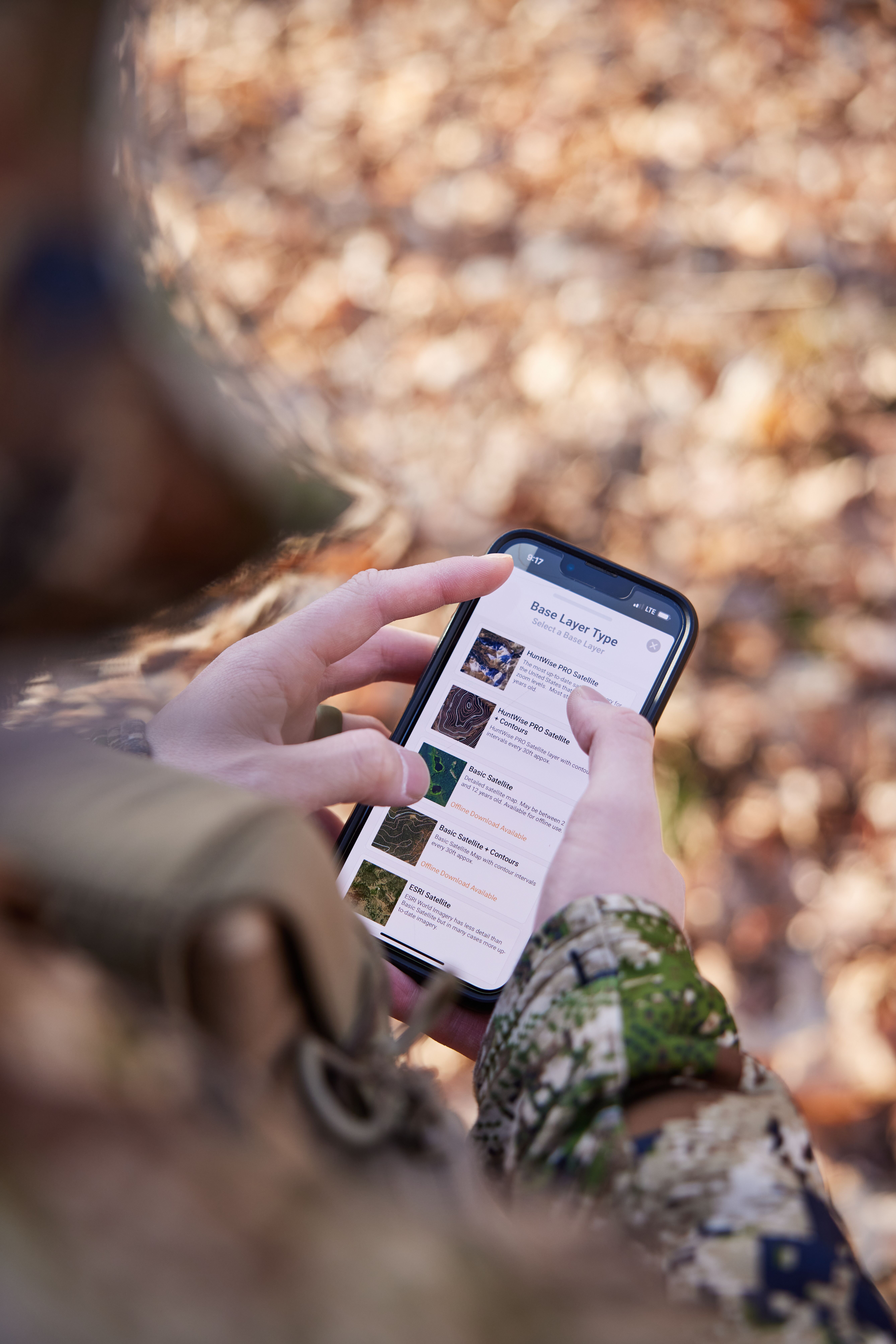 Close-up of a hand holding a phone with HuntWise on screen, hunting app and rifles for hunting concept.