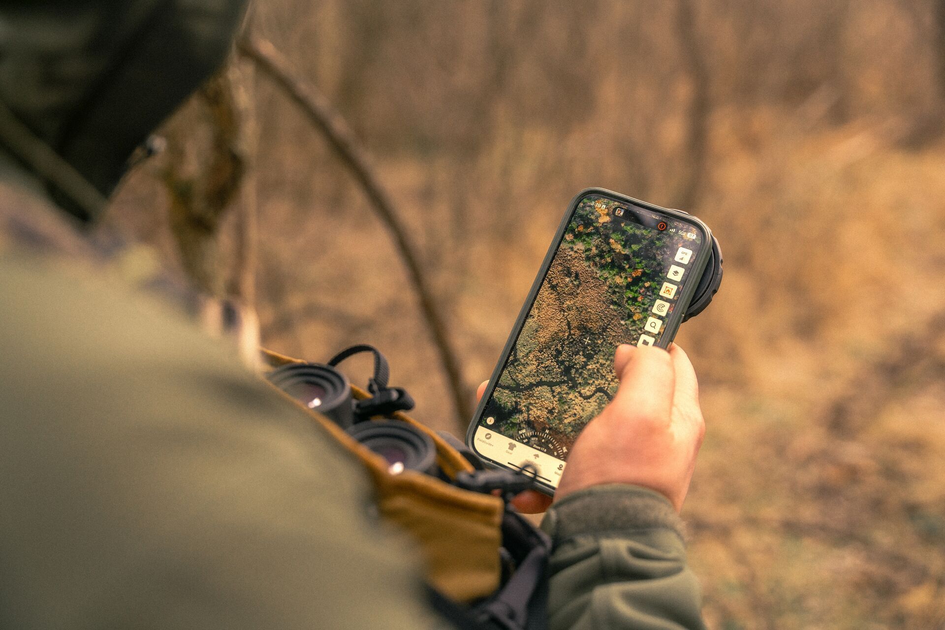 Close-up of a phone showing the HuntWise hunting app with a hunter holding phone.