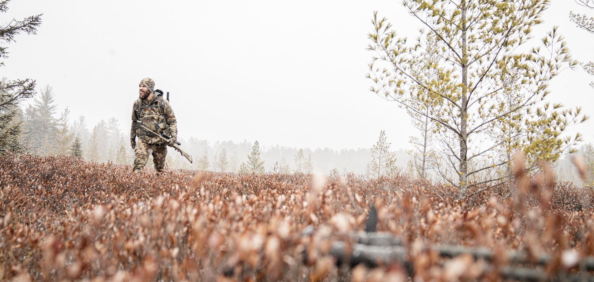 Hunter in camo with rifle treks terrain, best time to hunt moose concept.