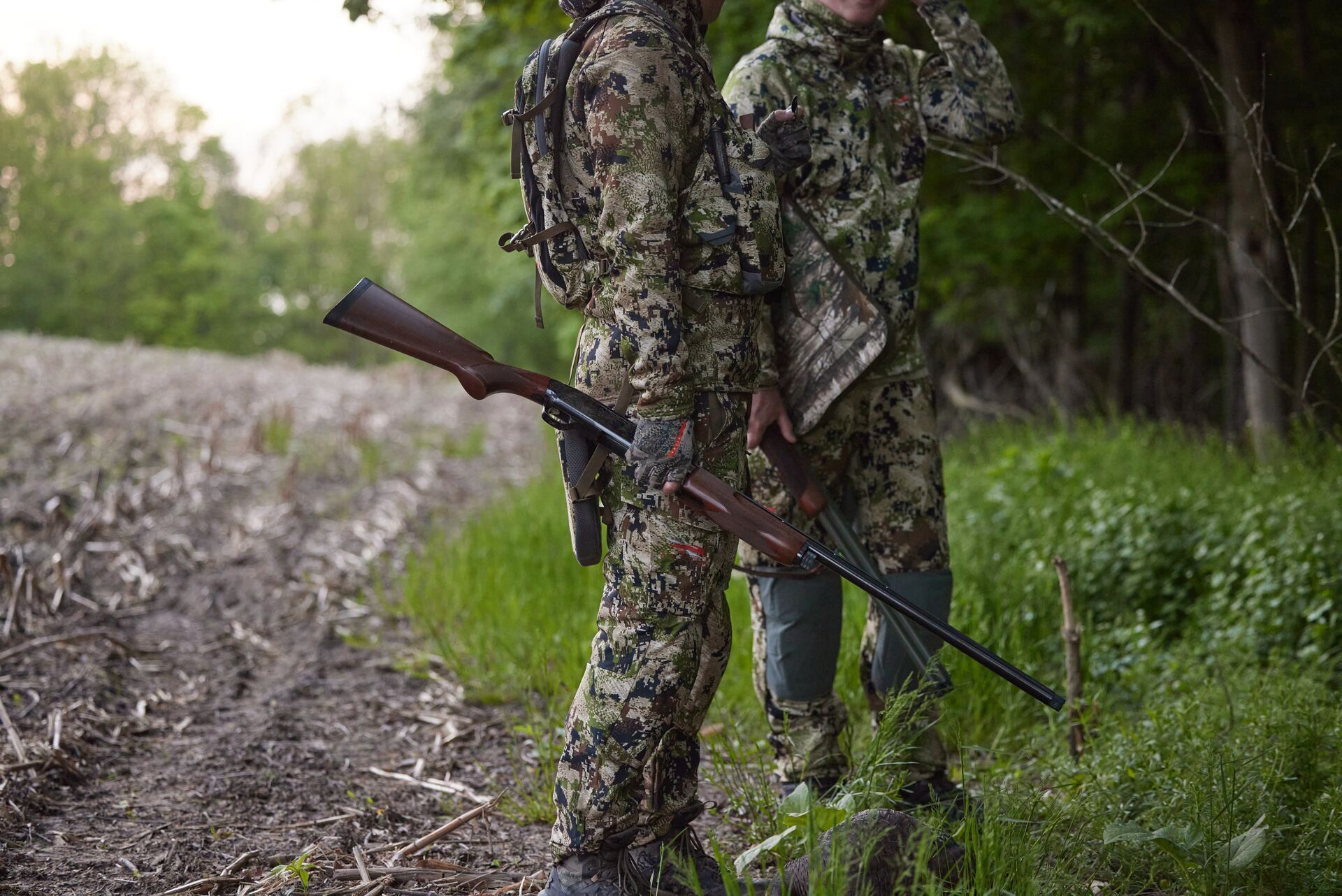 Hunters standing near woods with shotgun, 12 gauge vs 20 gauge concept.