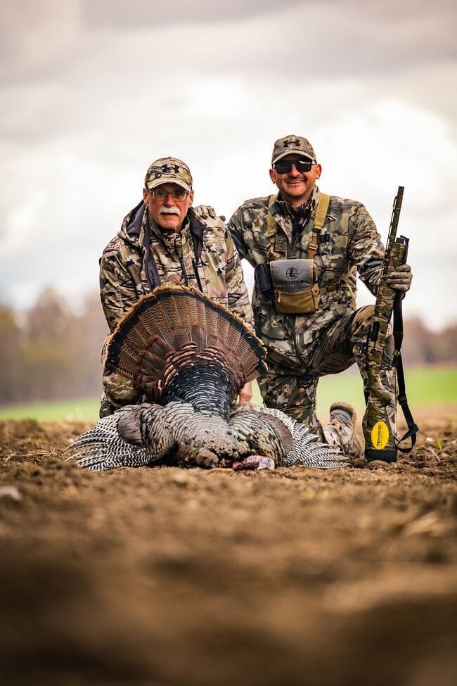 Two hunters smile and pose with turkey after hunt.