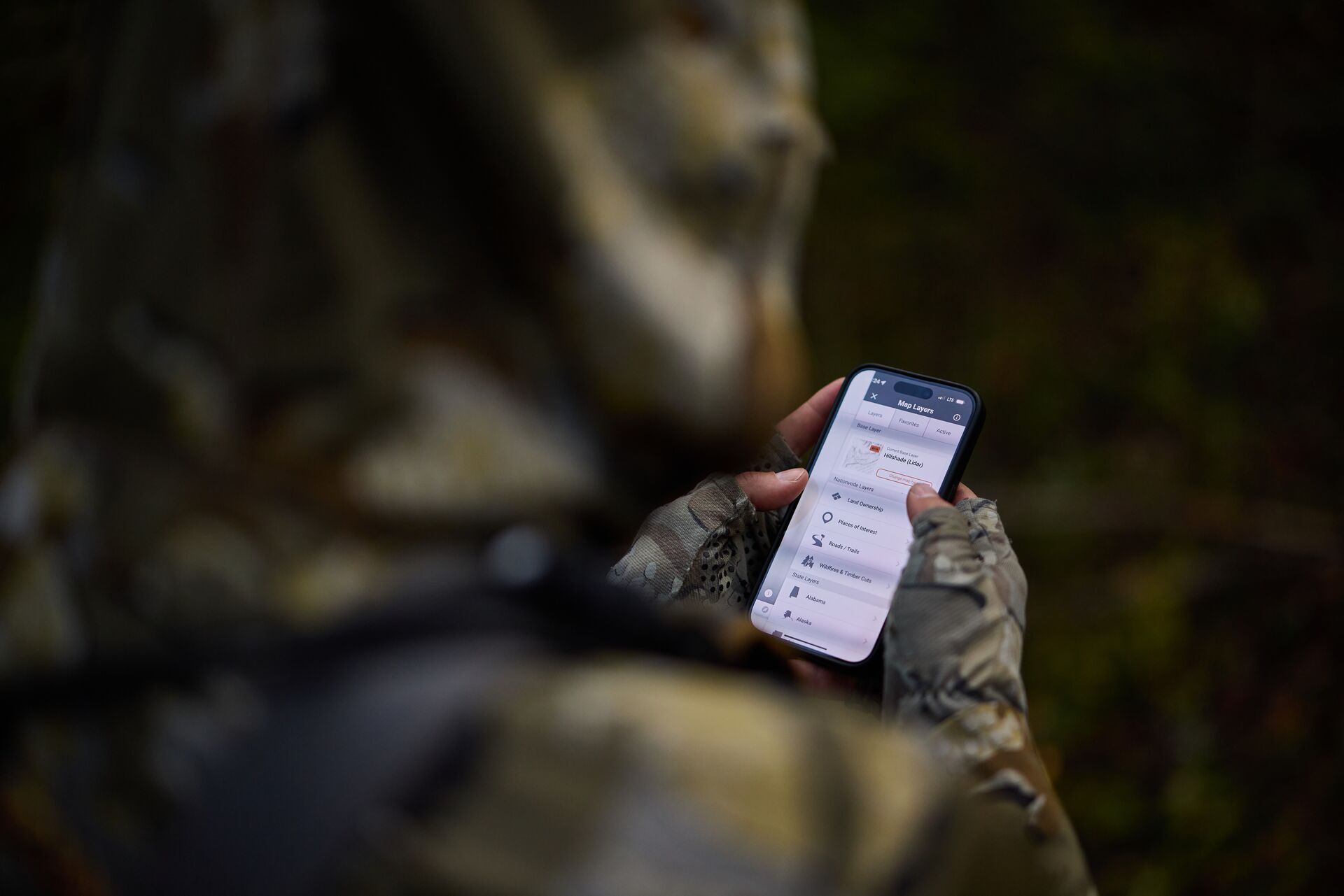 Hunter using phone showing HuntWise map layer options, hunting app with property lines concept.