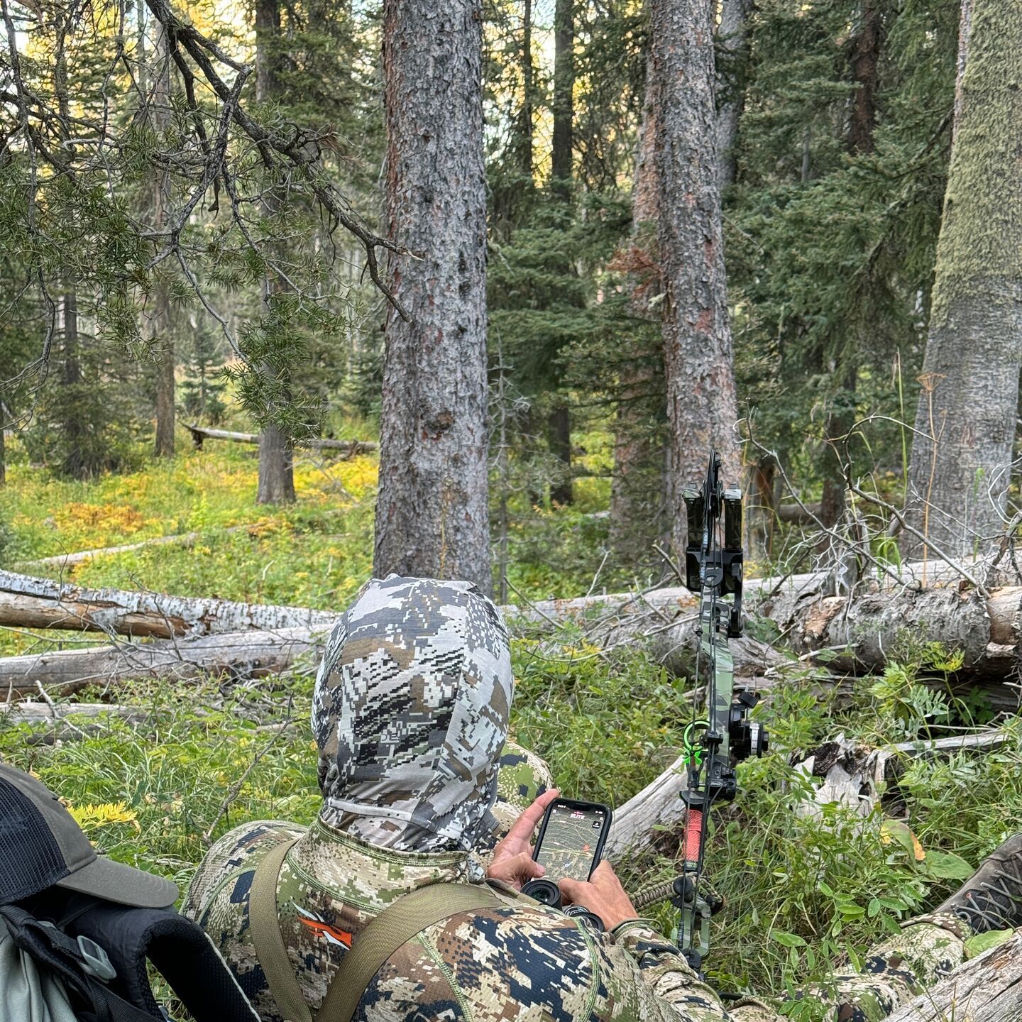 Hunter with gear pack, clothing, bow, and HuntWise on phone..
