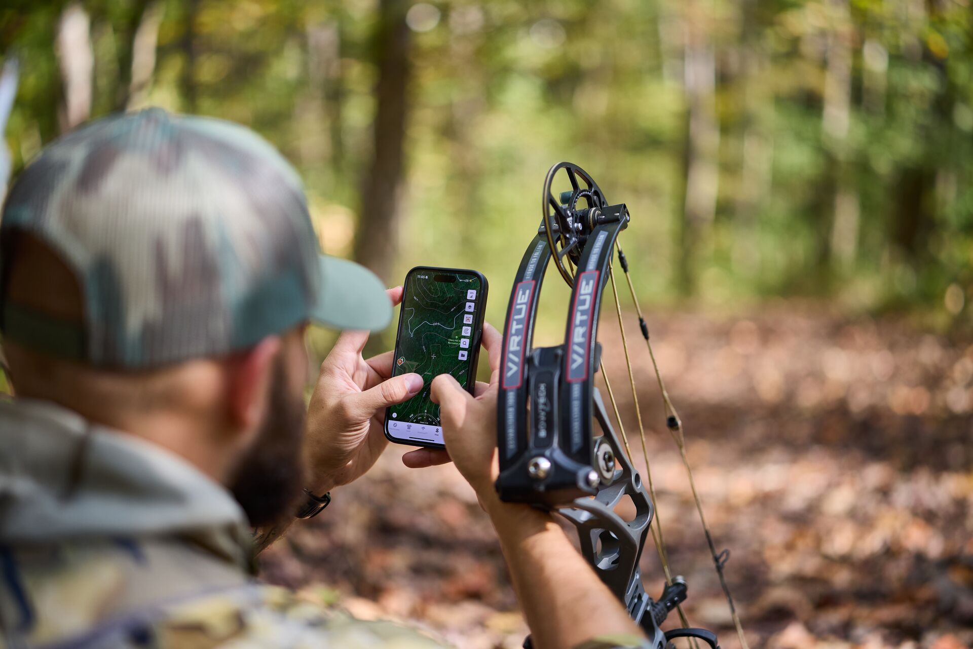 Hunter using the HuntWise app on phone with bow in woods.