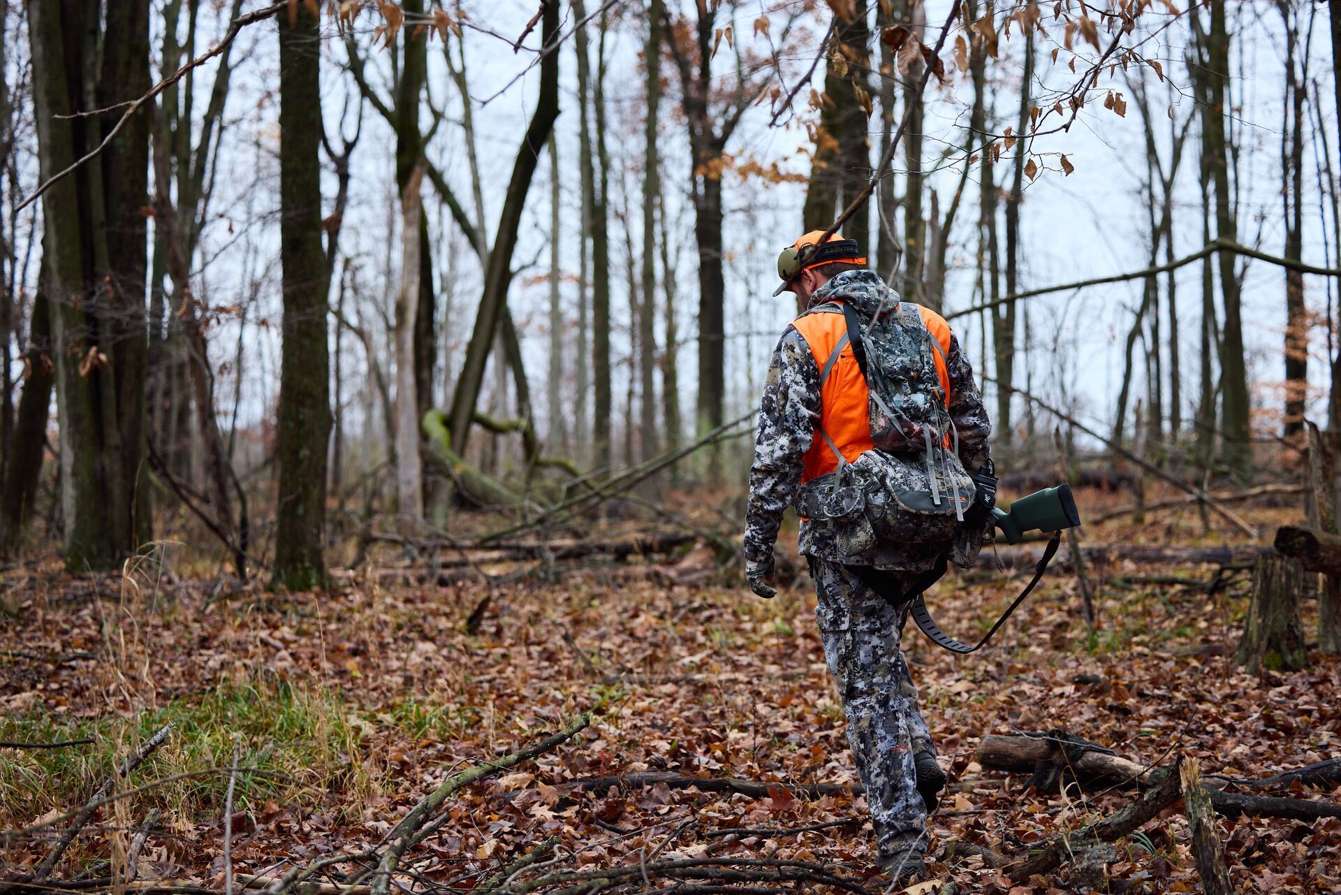 A deer hunter in the woods with a hunting rifle and gear.