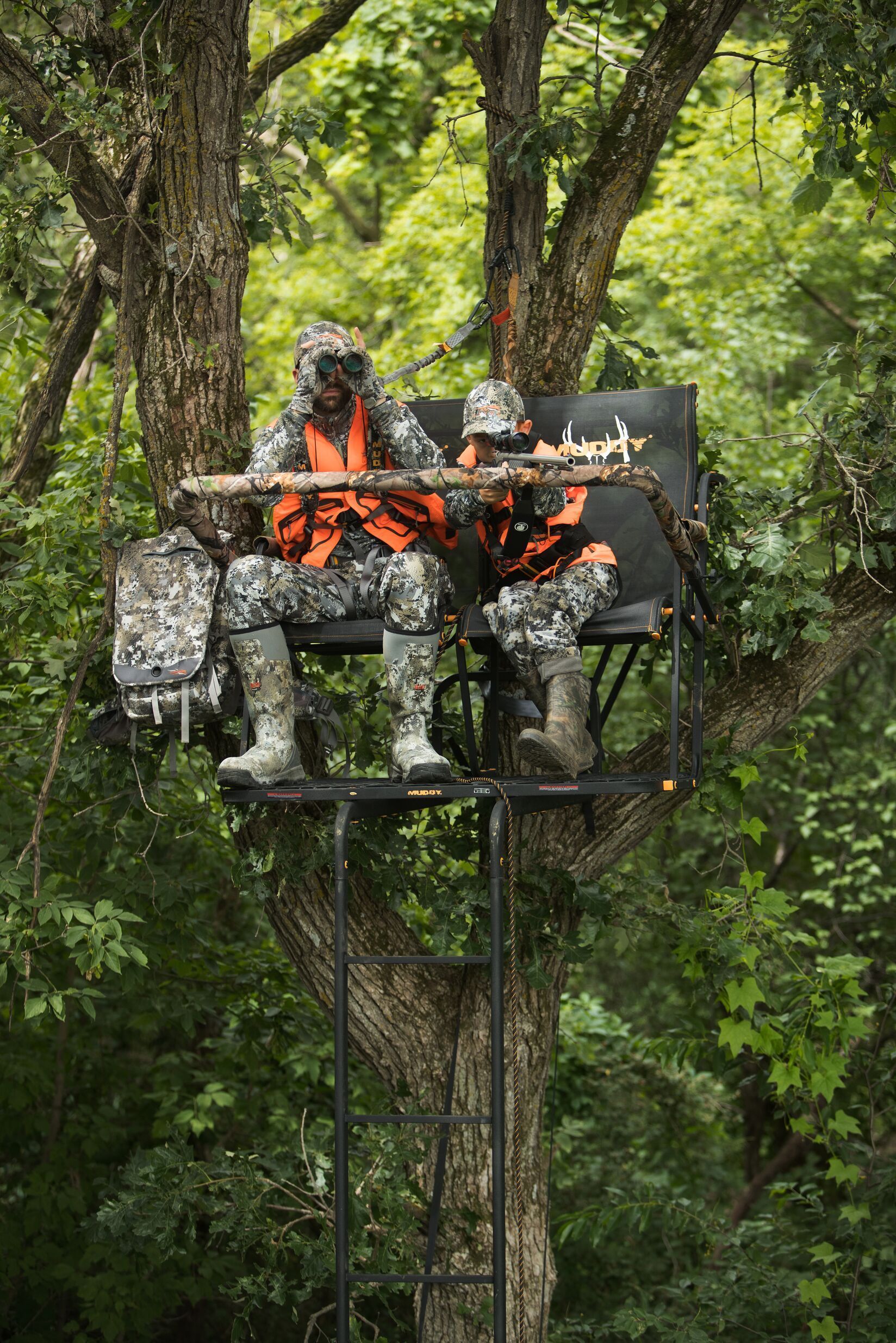 Man and boy in ladder stand during a hunt.