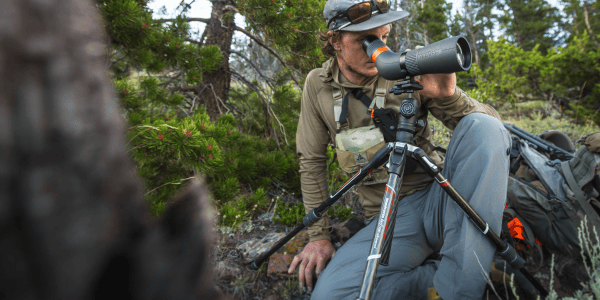 A hunter using a spotting scope on a tripod.