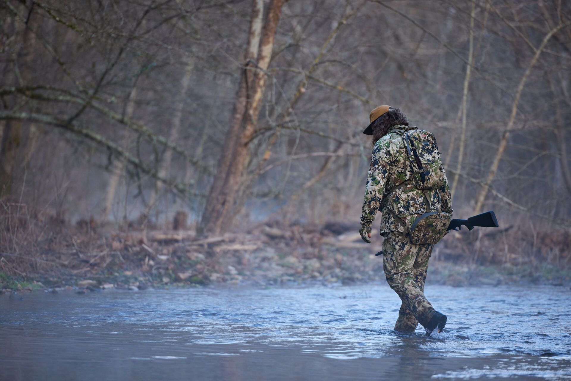 Hunter walking in creek, what is the best weather for turkey hunting concept.