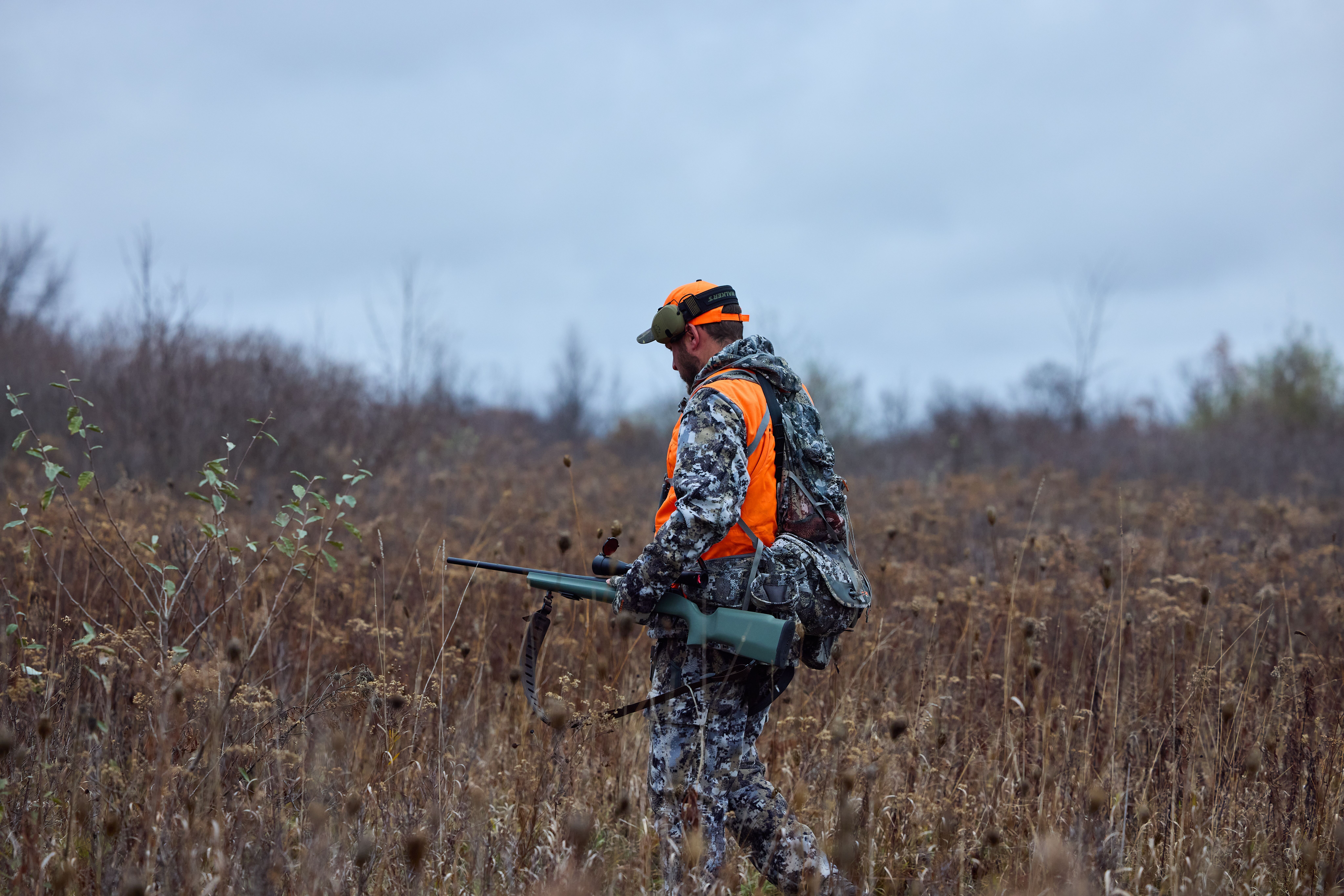 A hunter with a rifle walks through a field of tall brush, know land boundaries concept.