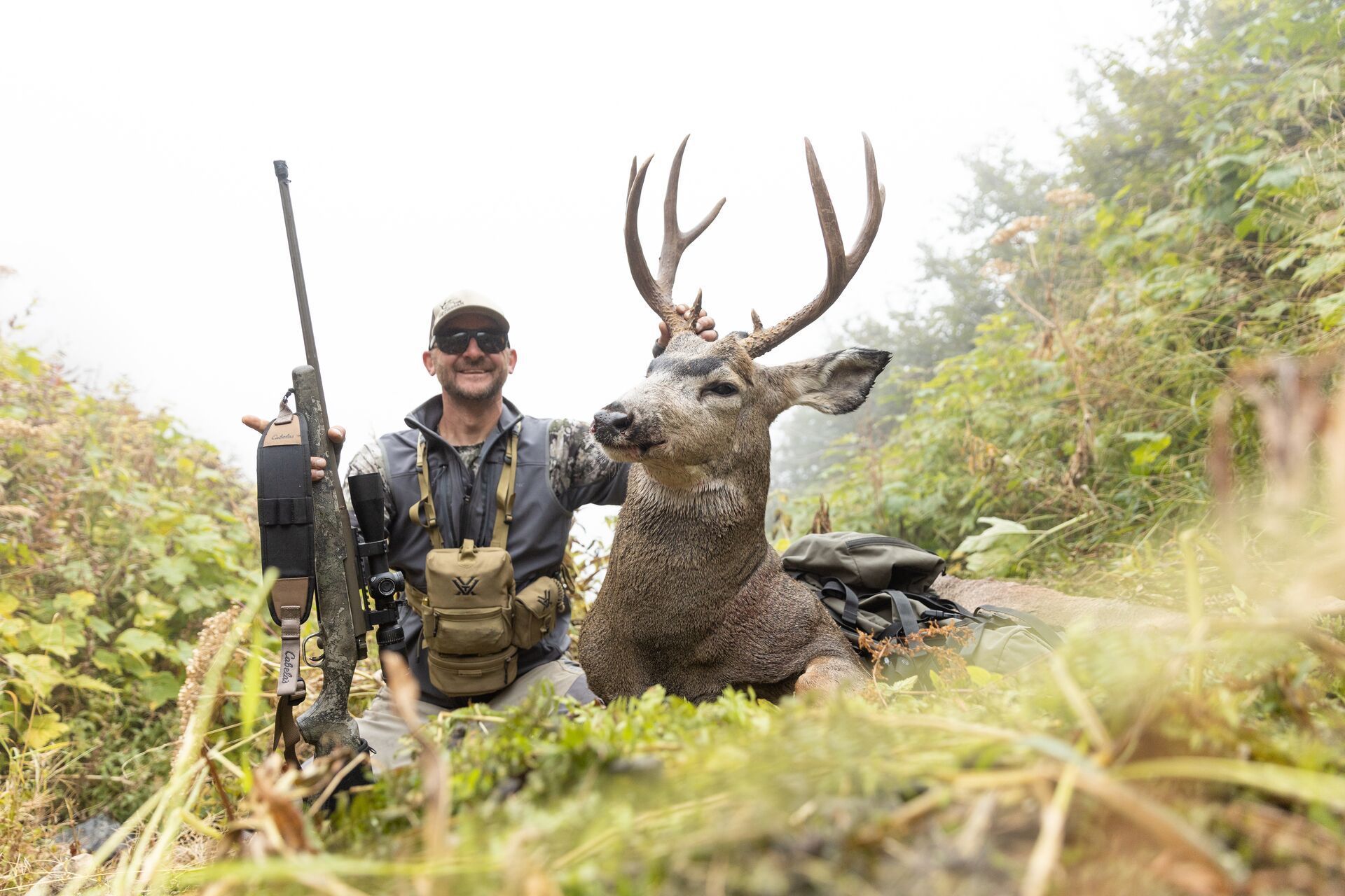 Smiling hunter with rifle and mule deer after hunt, mule deer hunting concept.