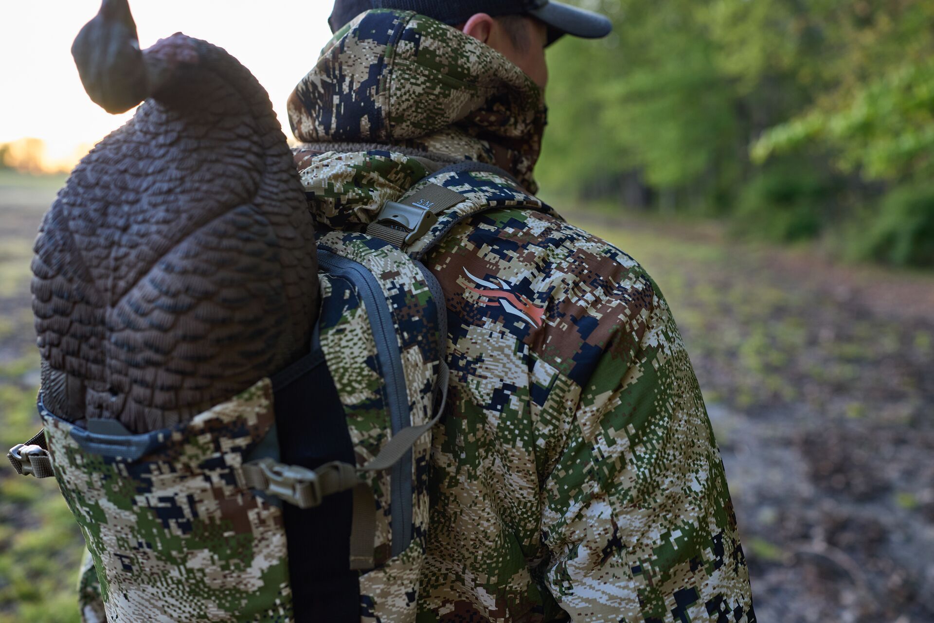 Turkey hunter in camo carries a turkey decoy on his back.