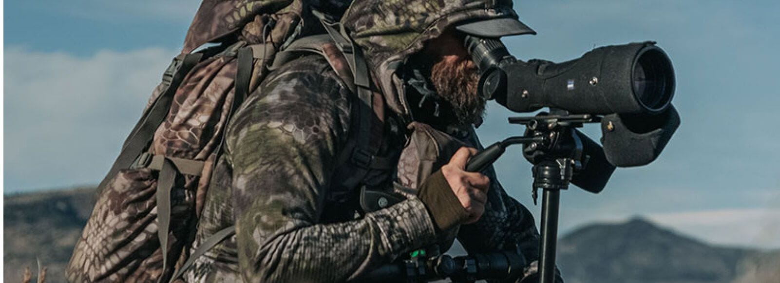 A hunter in camo with gear used a spotting scope.