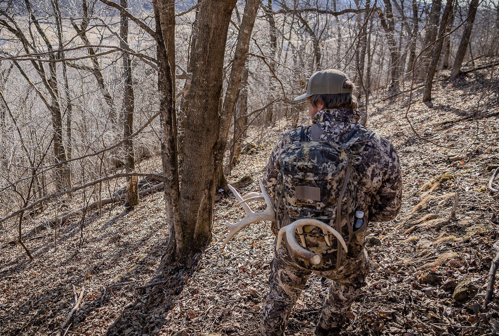 A hunter in camo in the woods carrying deer antlers on his pack, using deer calls concept.