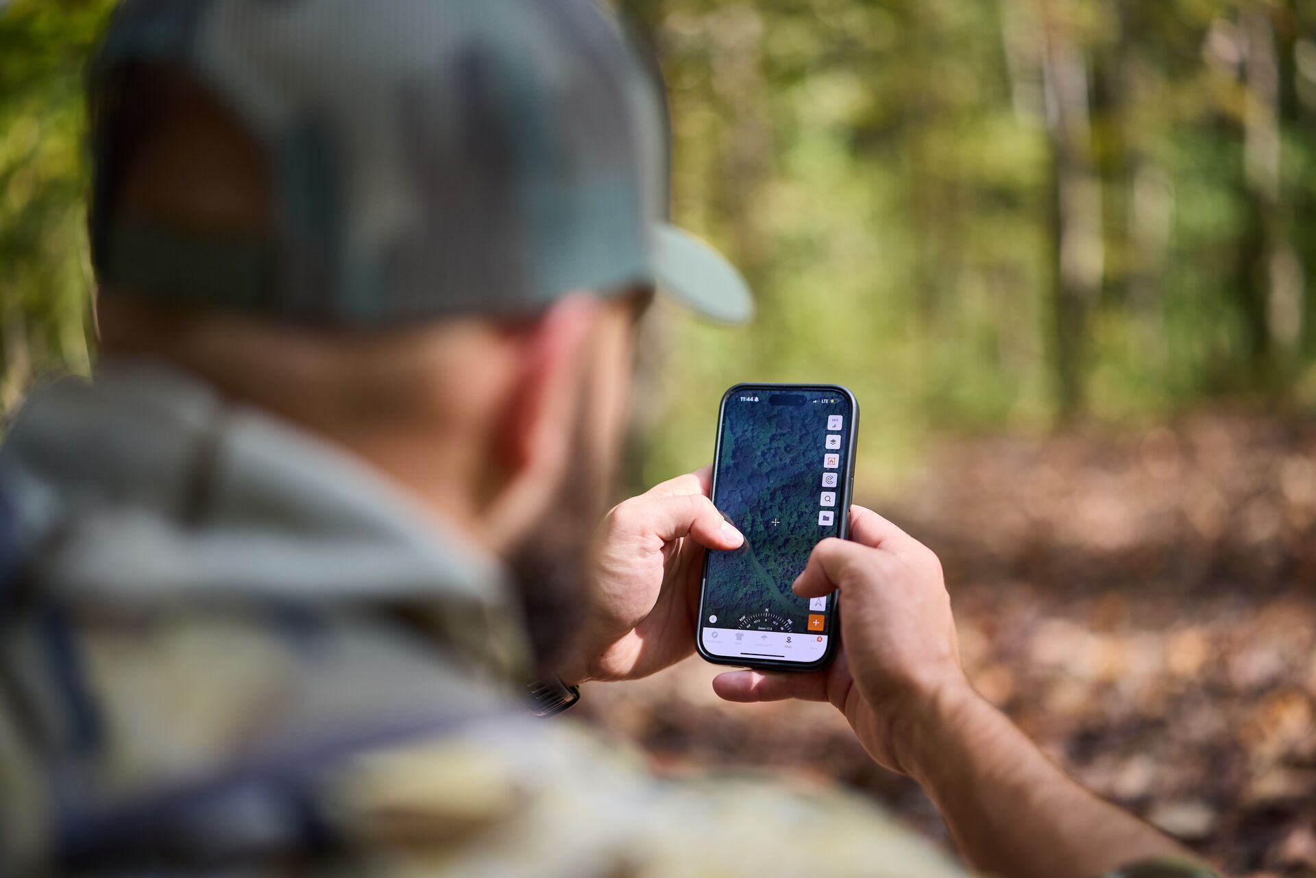 Hunter in the woods using HuntWise app on phone, rabbit trapping concept.