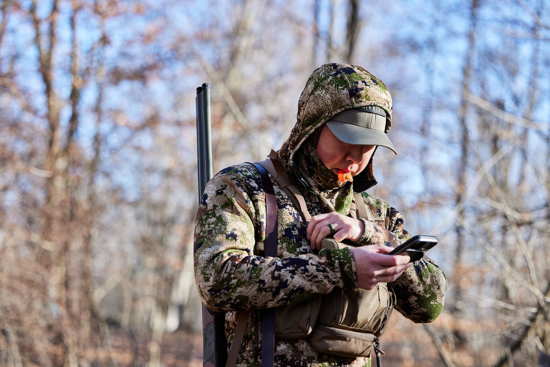 A hunter in camo uses a phone with the HuntWise app for turkey hunting.