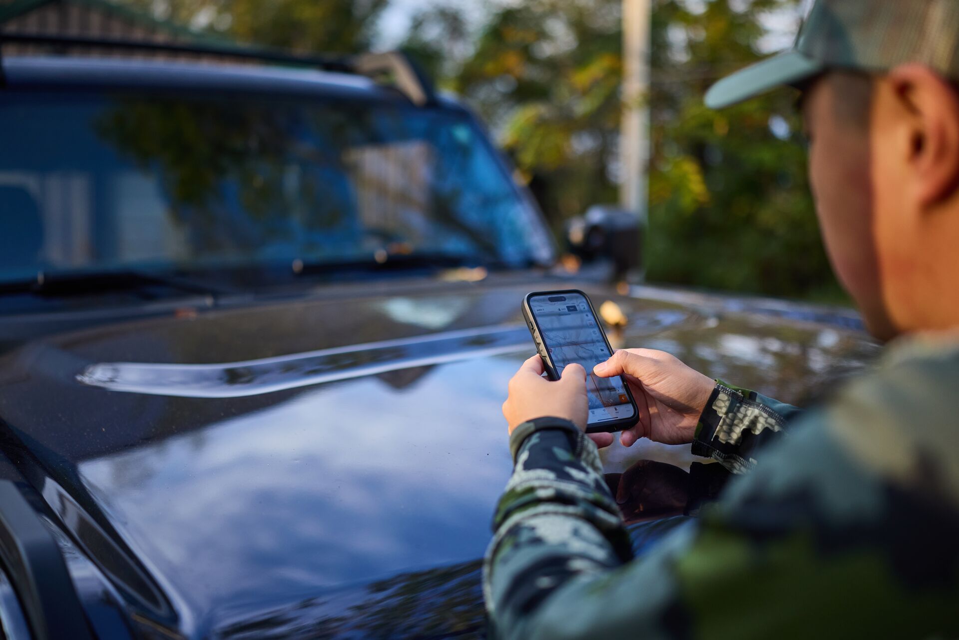 Hunter leans on truck using HuntWise on phone, how to use hunting app concept.