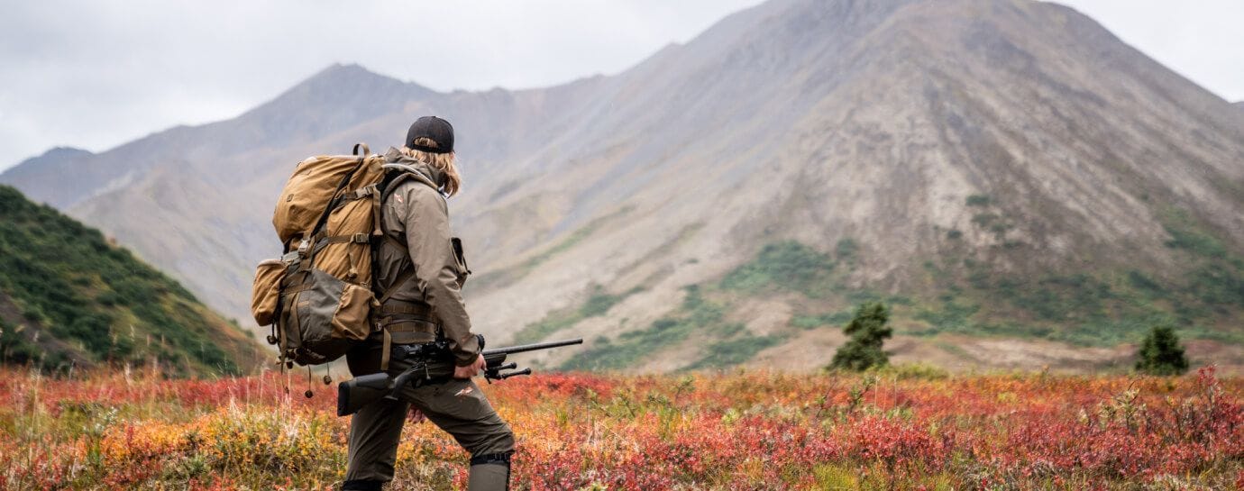 A hunter with a large pack and a rifle in the mountains, get fit for a bear hunt concept.