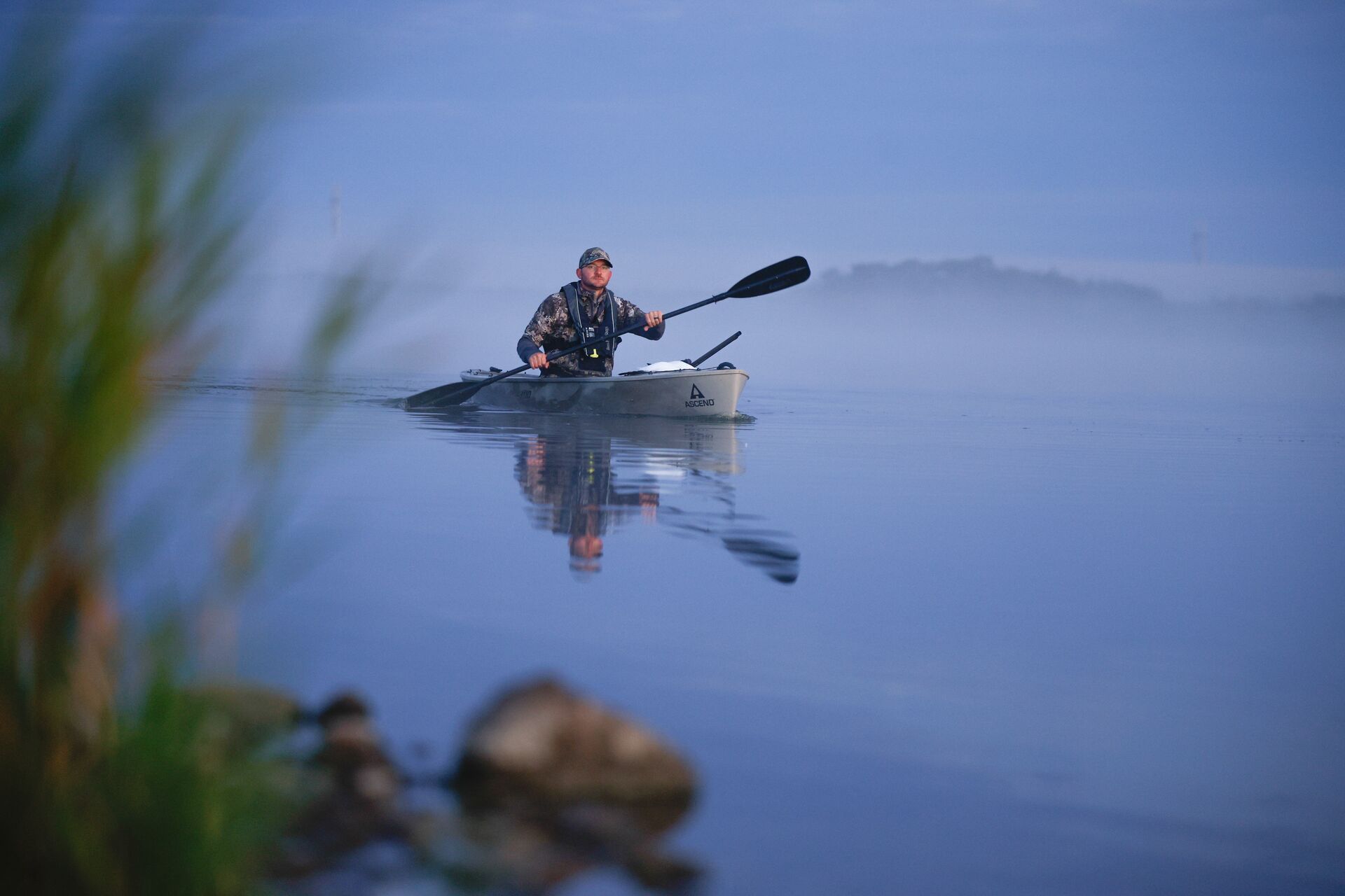 A hunter paddles a canoe on calm water.