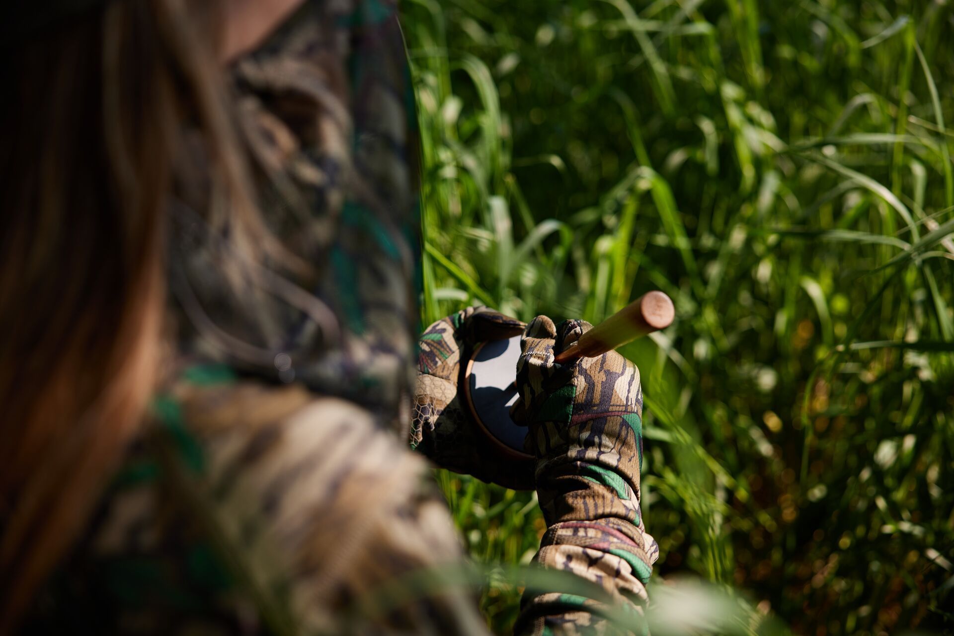 Close-up of a hunter using a turkey slate call while sitting in the brush.