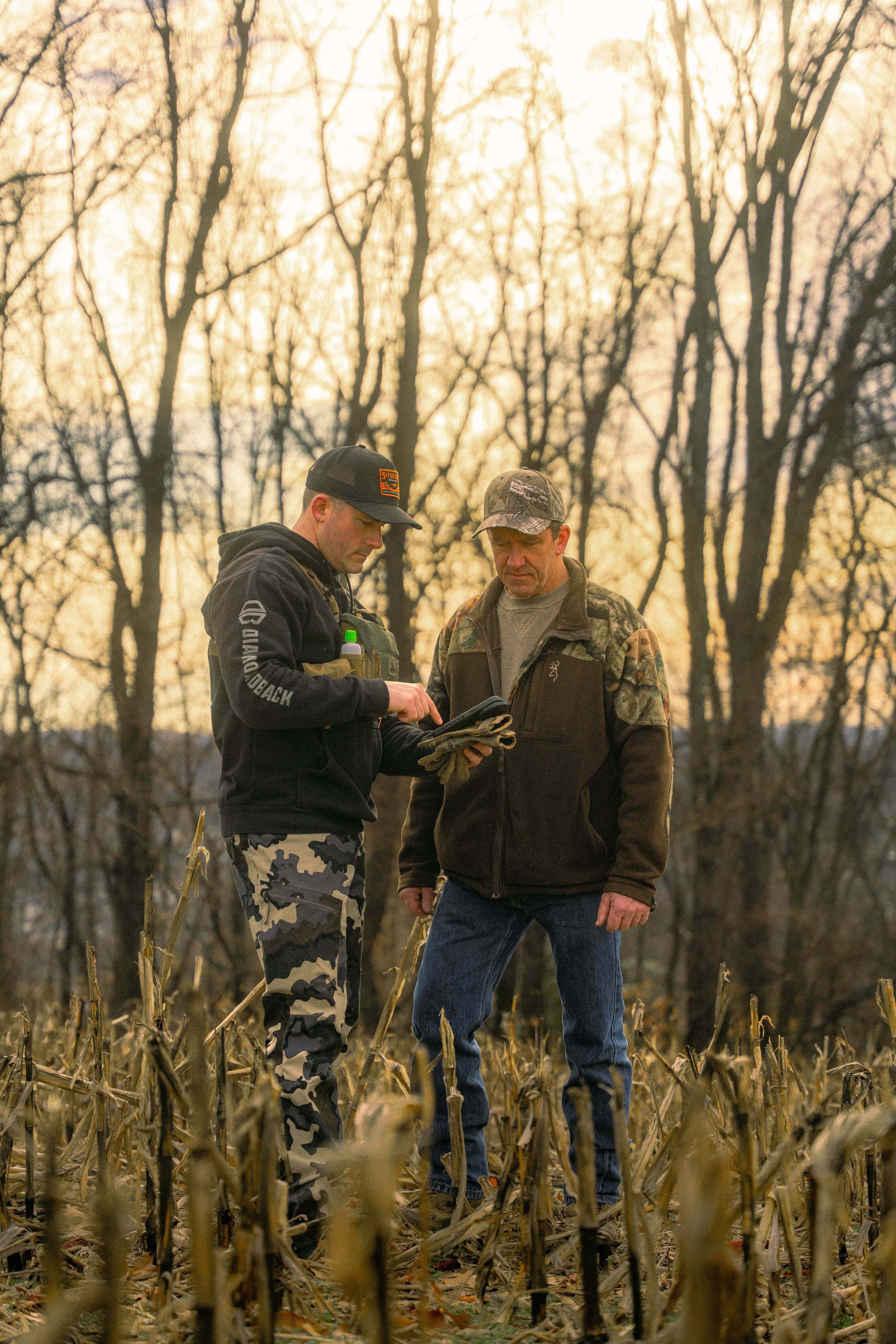 Two men in field looking at phone, coyote tracking concept.
