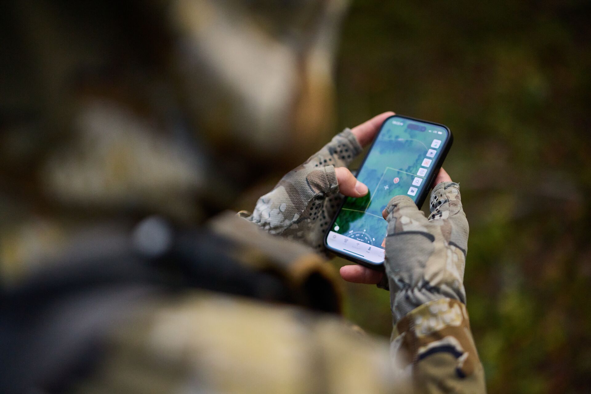 Hunter holds phone showing HuntWise terrain view, escouting elk concept.
