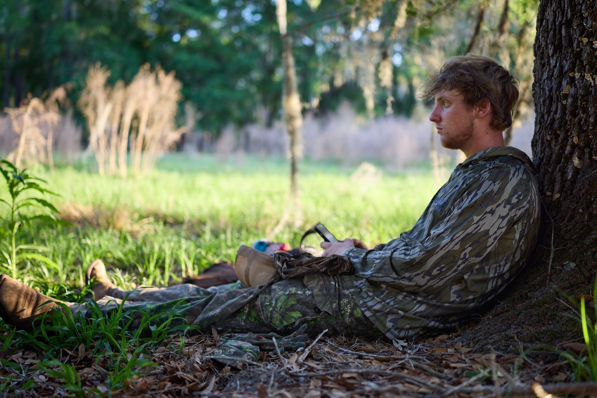 Hunter sits against a tree hot and tired, hunting in summer concept.