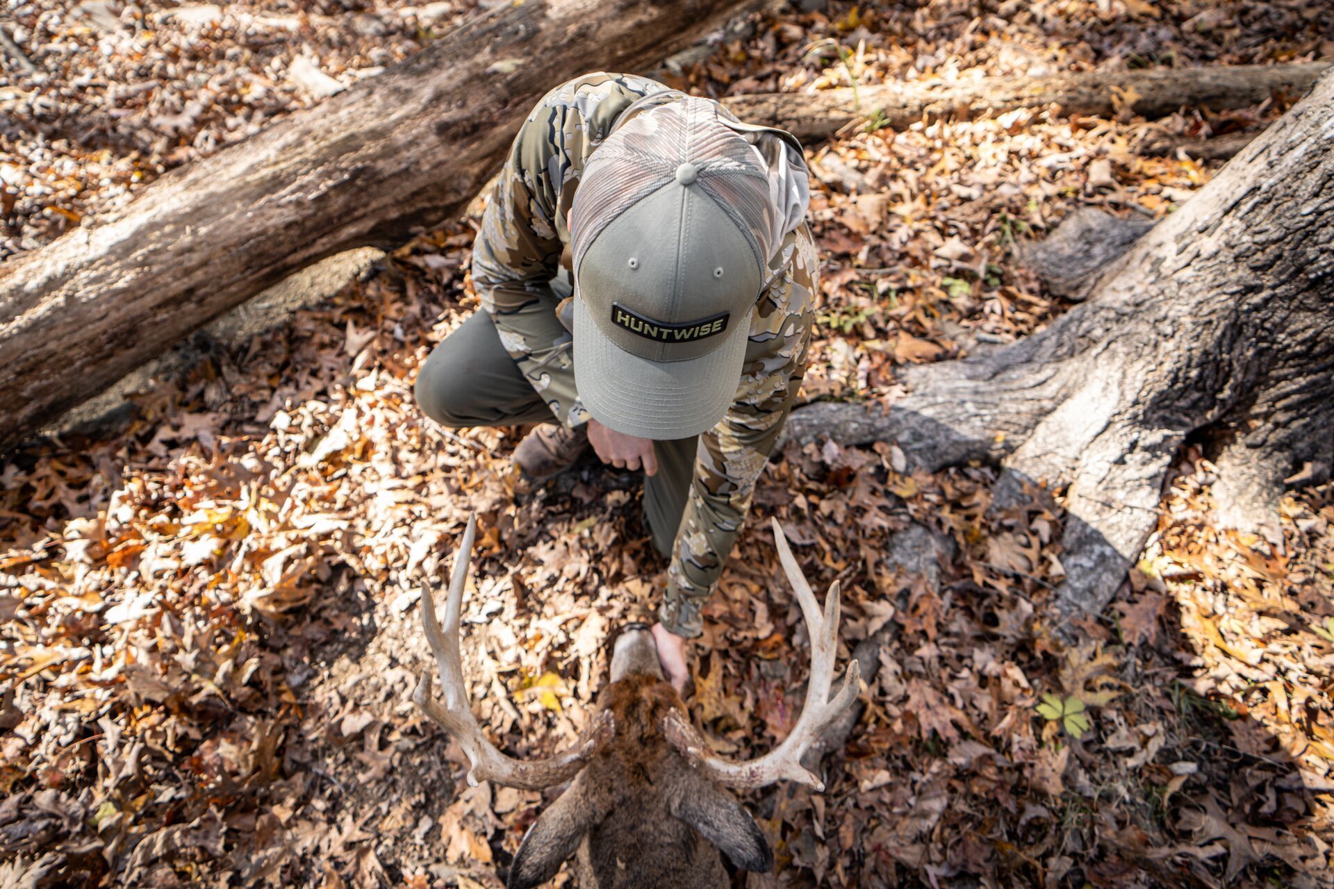 Hunter wearing HuntWise hat with buck on ground, public land hunting app concept.