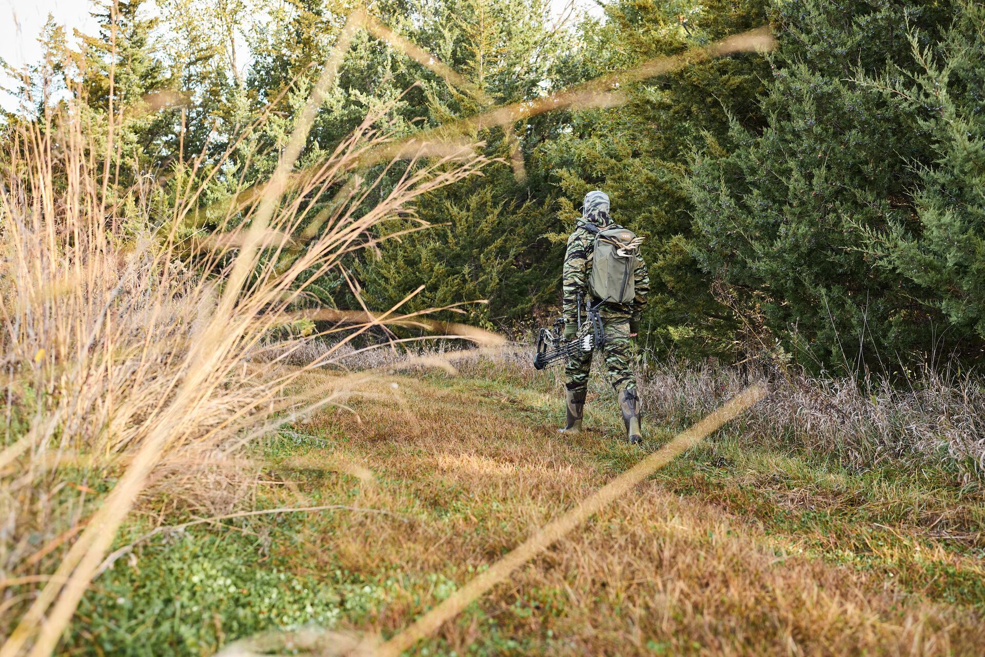 Hunter with gear walks near trees, how to use WindCast for hunting concept.