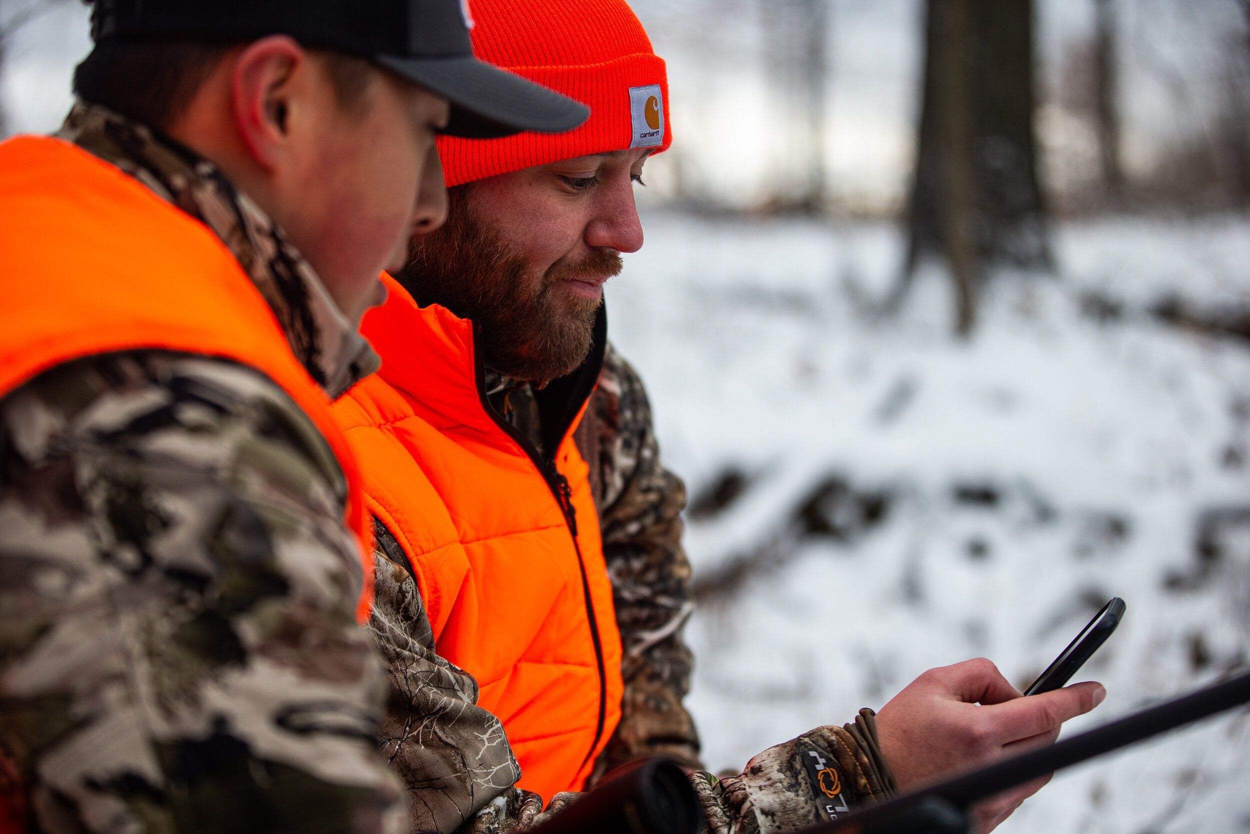 Two hunters in blaze orange look at a phone, use HuntWise for winter rabbit hunts concept.