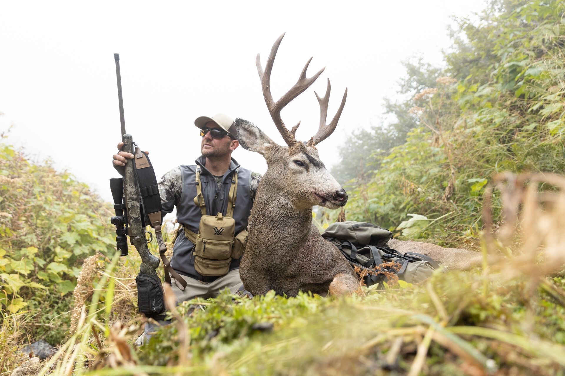 Hunter with large caliber bolt action rifle and deer after hunt.