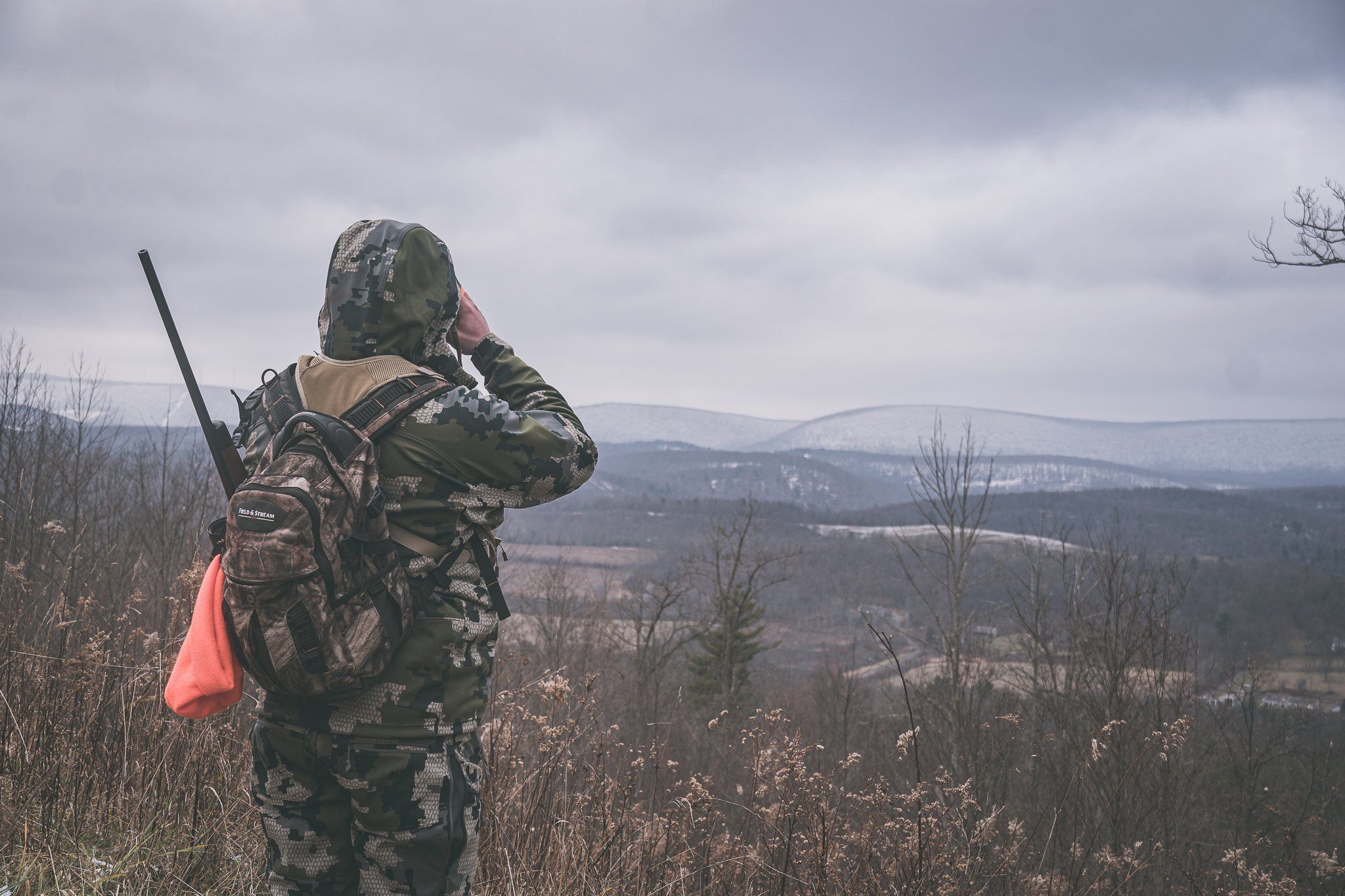 A hunter in camo on a hill using binoculars, prepping for an elk hunt in Wyoming concept.