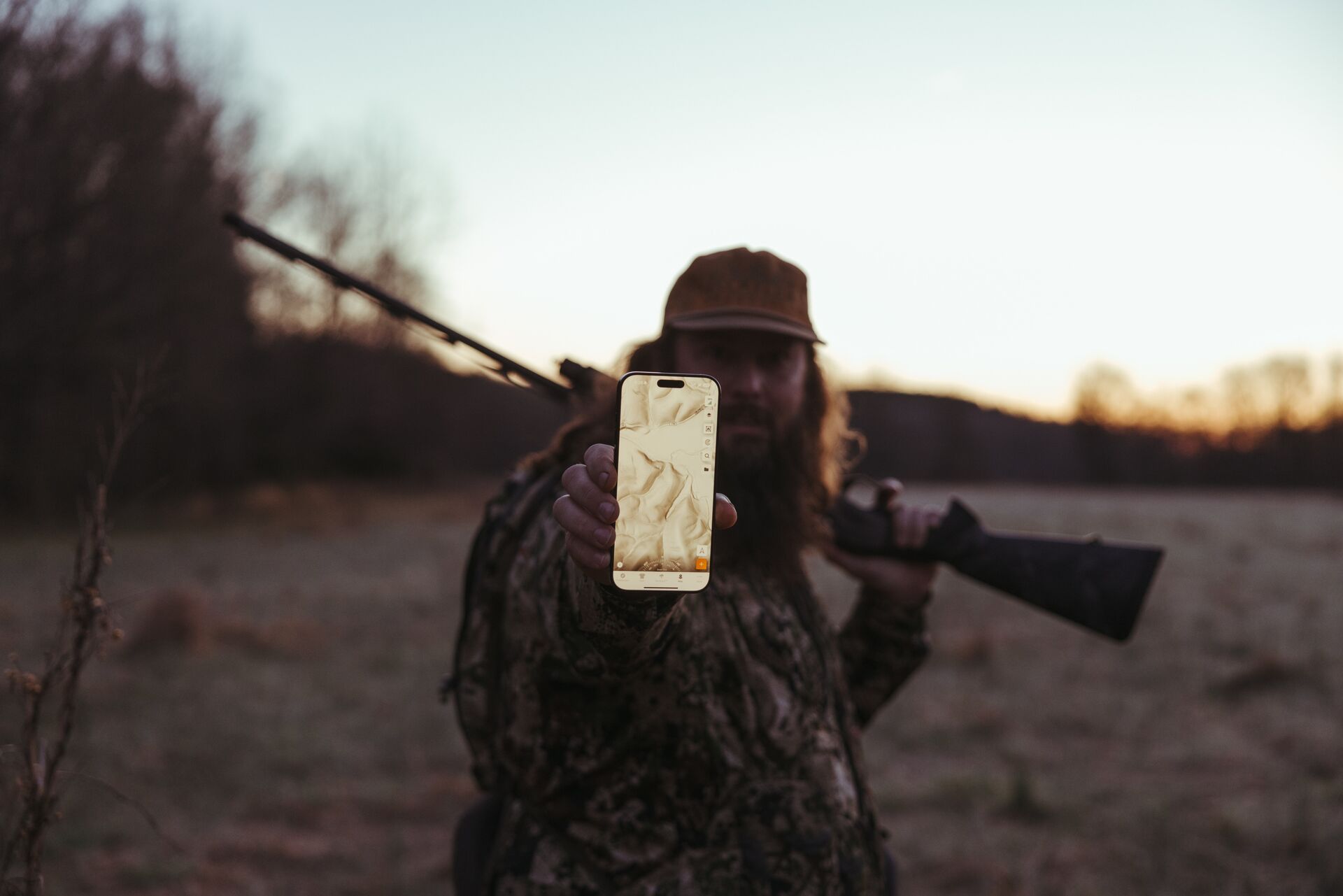 Hunter with firearm holds up a phone showing HuntWise LiDAR map on screen.