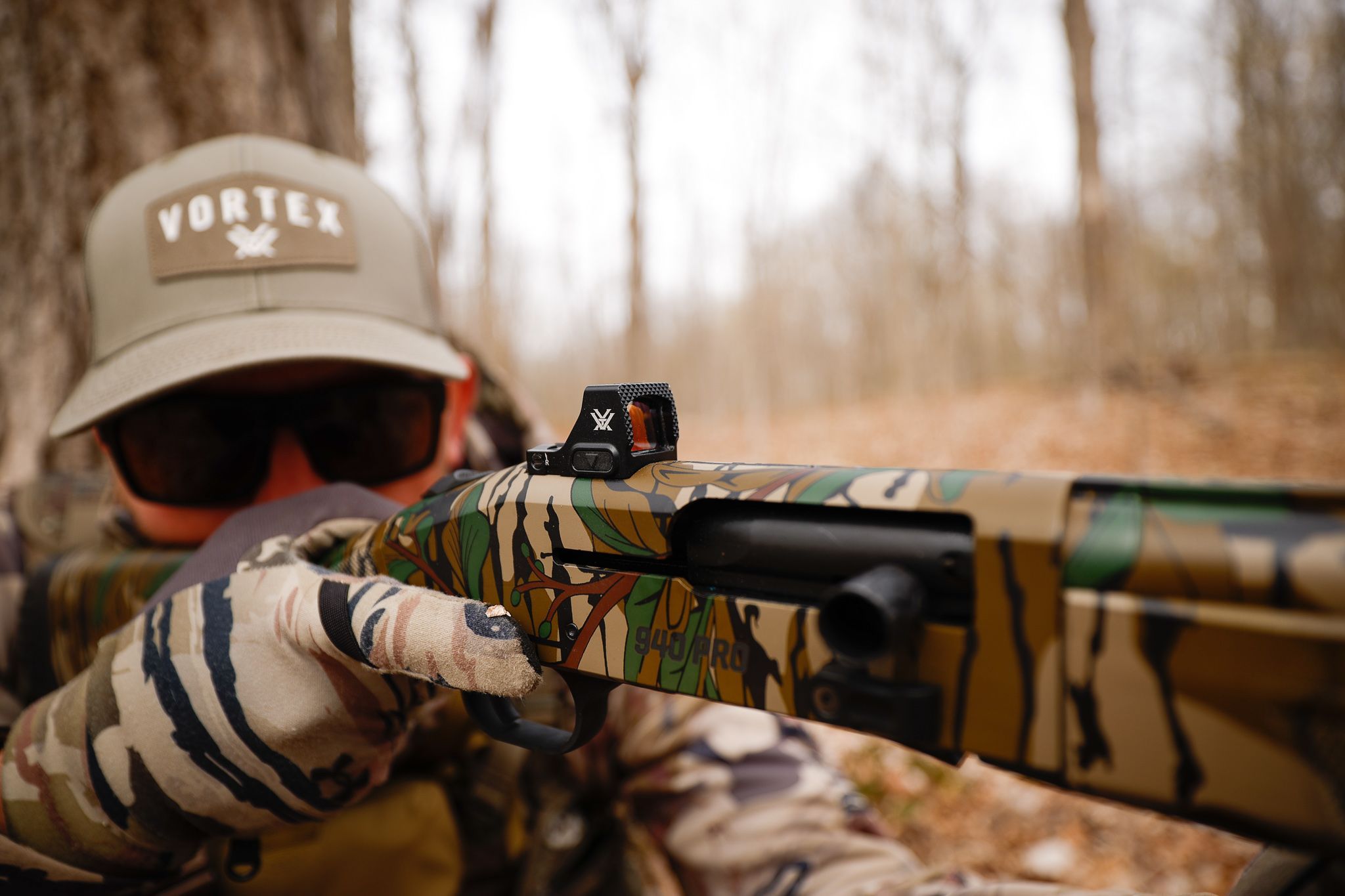 A hunter in turkey camo aims a shotgun.