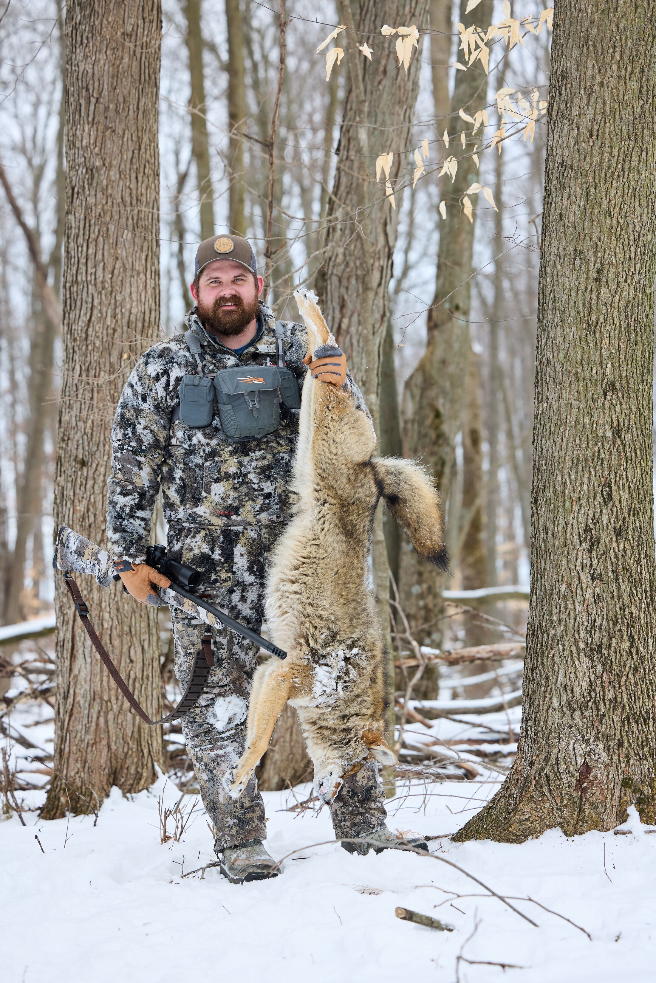 Hunter smiles and holds a coyote up after a hunt, how to hunt coyote concept.